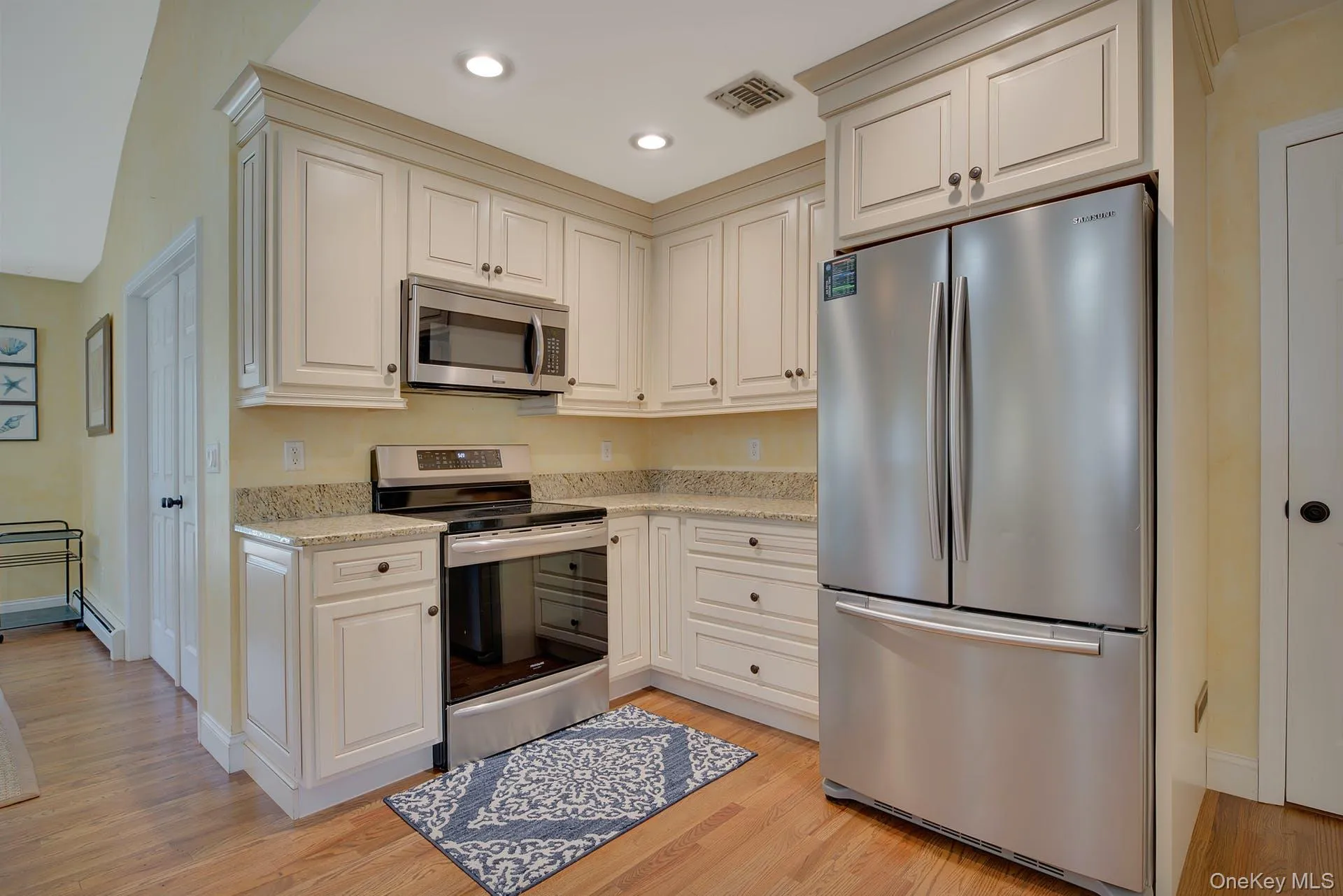 Kitchen featuring appliances with stainless steel finishes, light stone counters, light wood-type flooring, recessed lighting, and baseboard heating Kitchen featuring appliances with stainless steel finishes, light stone counters, light wood-type flooring, recessed lighting, and baseboard heating