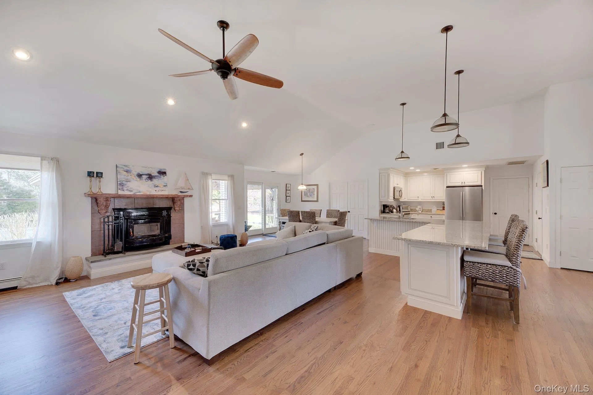 Living area featuring light wood-style floors, recessed lighting, a ceiling fan, a fireplace, and high vaulted ceiling Living area featuring light wood-style floors, recessed lighting, a ceiling fan, a fireplace, and high vaulted ceiling