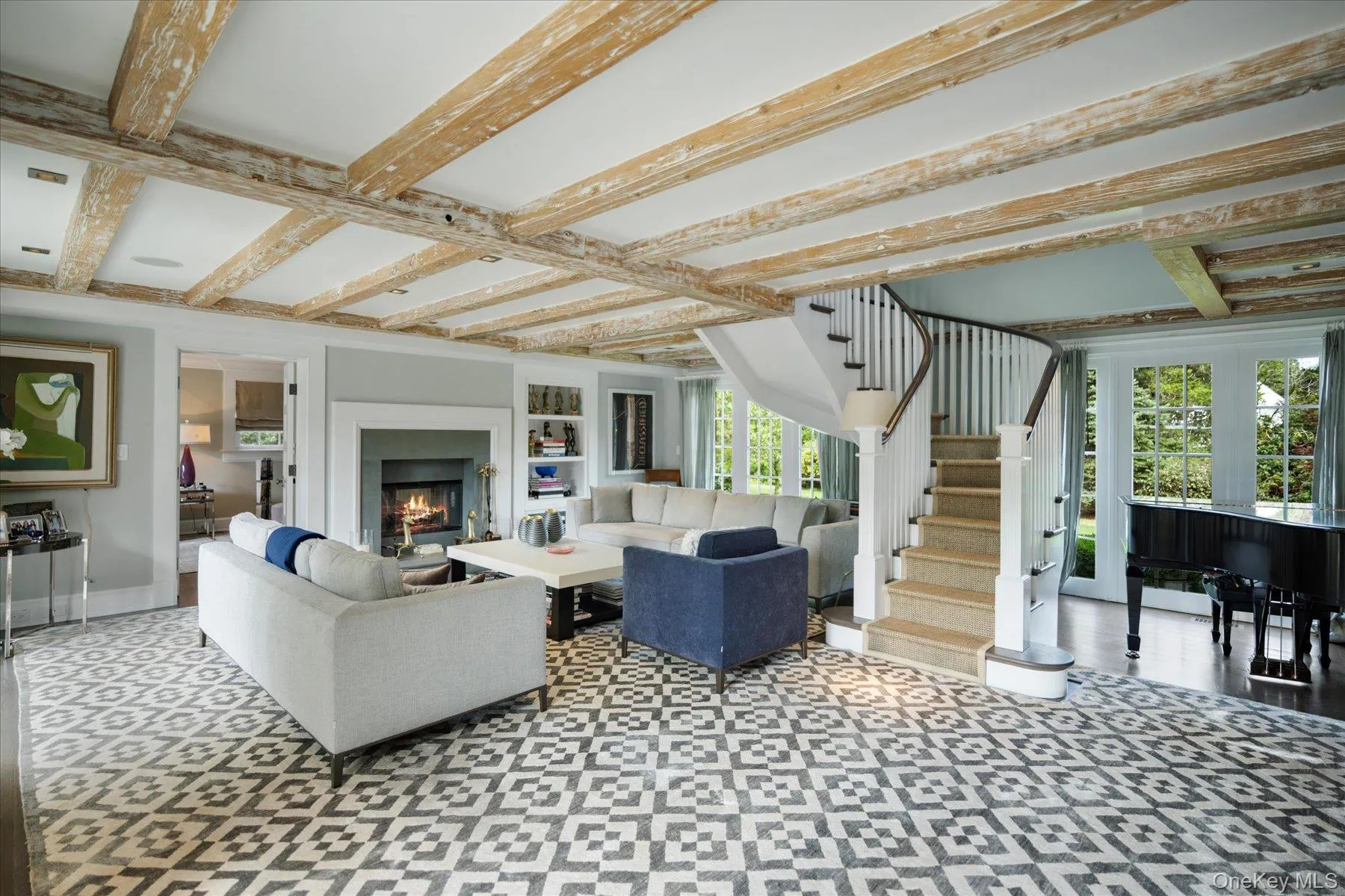 Living room featuring beamed ceiling, a lit fireplace, and stairway Living room featuring beamed ceiling, a lit fireplace, and stairway