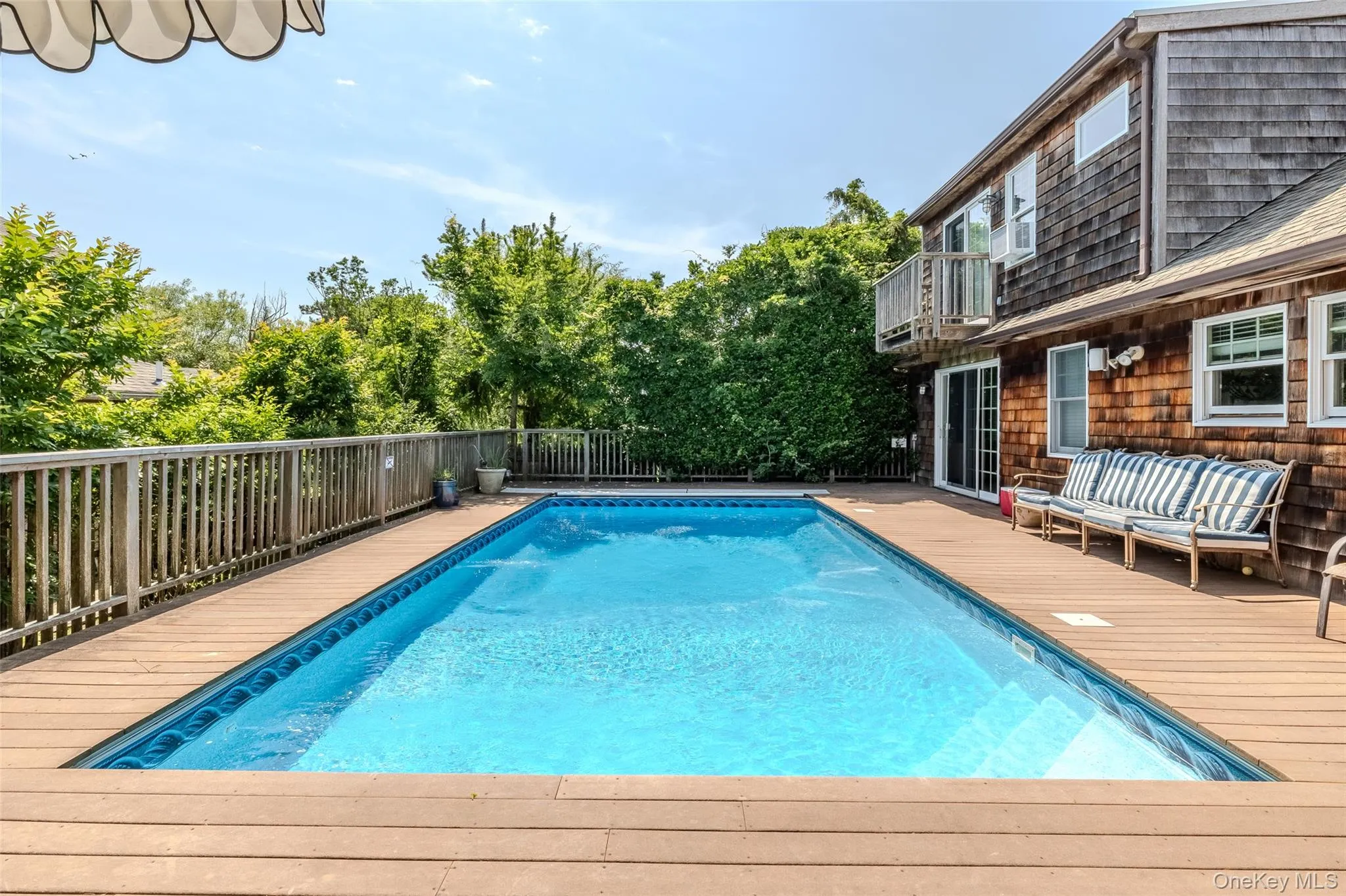 View of swimming pool featuring a wooden deck, a fenced backyard, and view of scattered trees View of swimming pool featuring a wooden deck, a fenced backyard, and view of scattered trees