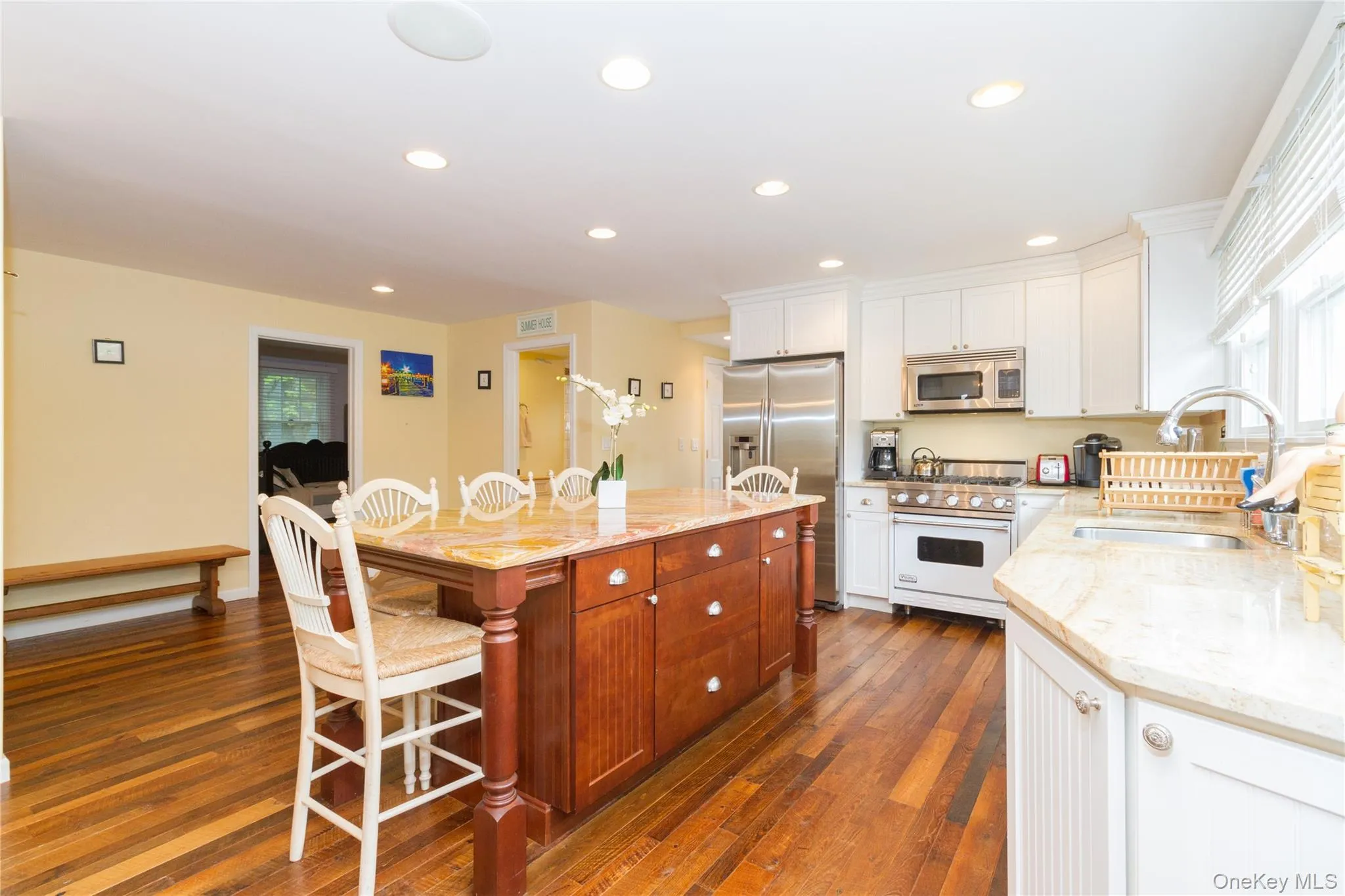 Kitchen with a kitchen bar, white cabinetry, light stone counters, stainless steel appliances, and dark wood-type flooring Kitchen with a kitchen bar, white cabinetry, light stone counters, stainless steel appliances, and dark wood-type flooring