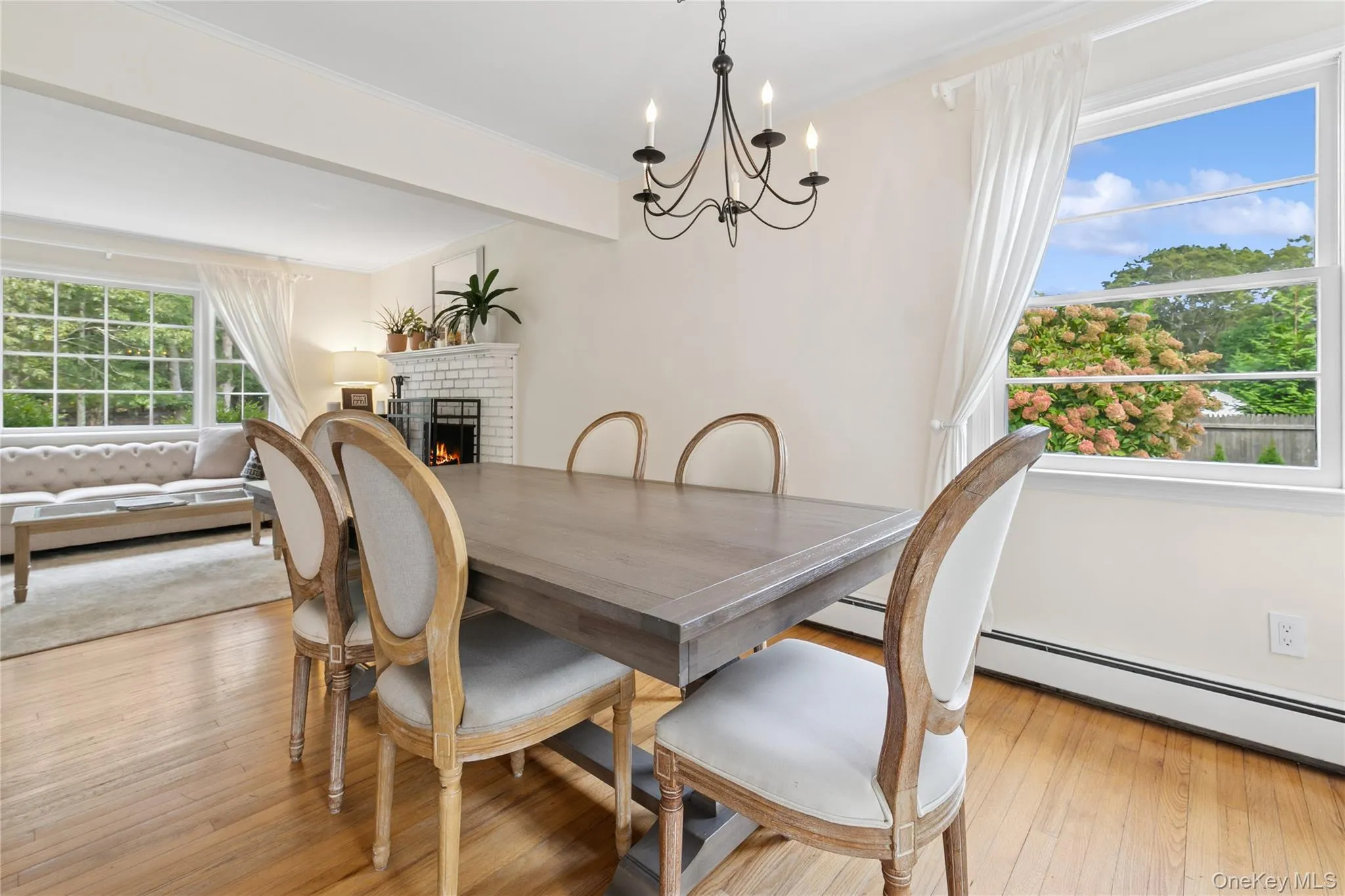 Dining space with a brick fireplace, a chandelier, light wood-type flooring, beamed ceiling, and baseboard heating Dining space with a brick fireplace, a chandelier, light wood-type flooring, beamed ceiling, and baseboard heating