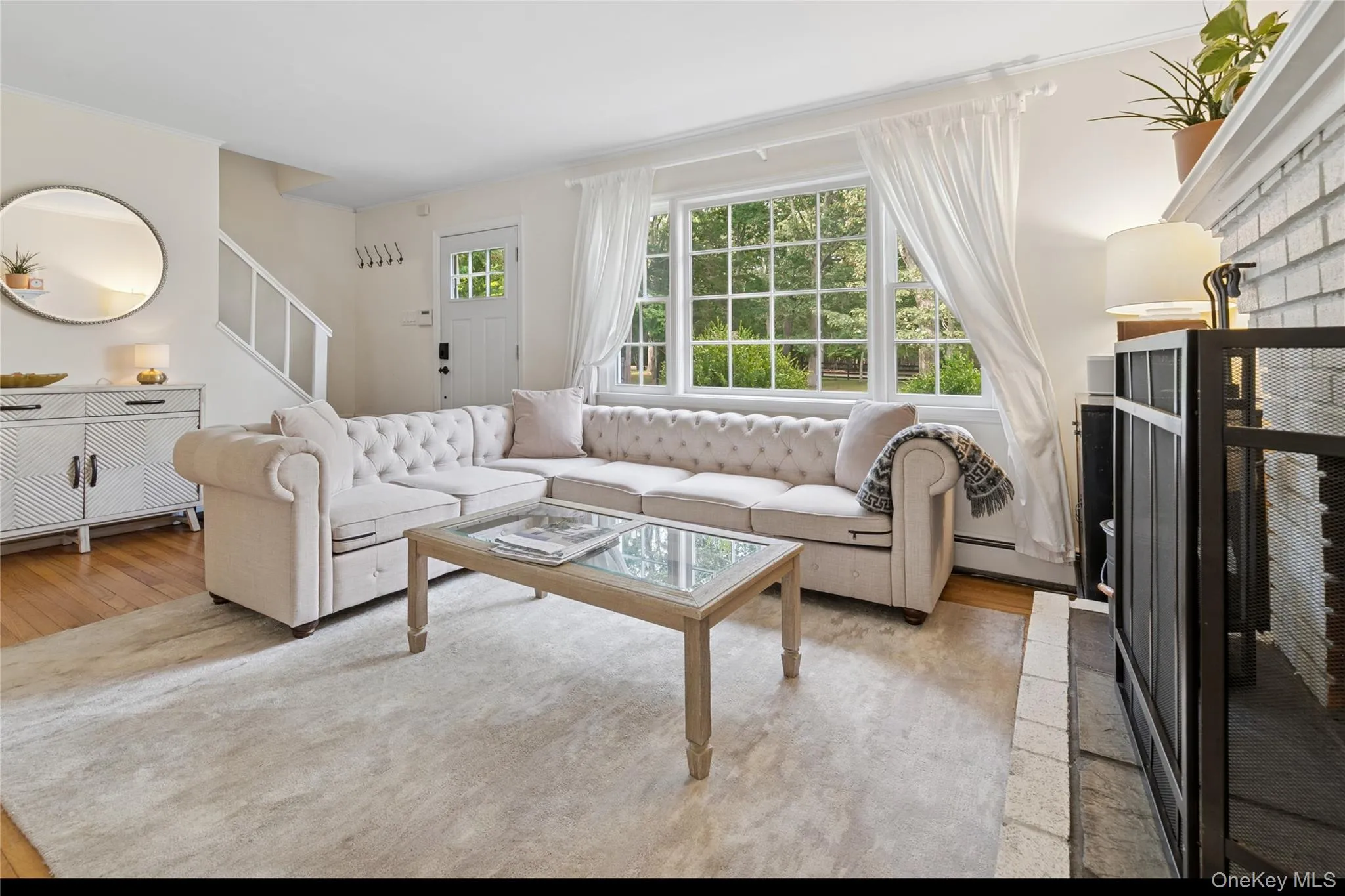 Living area featuring a brick fireplace, stairs, a baseboard radiator, light wood-type flooring, and crown molding Living area featuring a brick fireplace, stairs, a baseboard radiator, light wood-type flooring, and crown molding