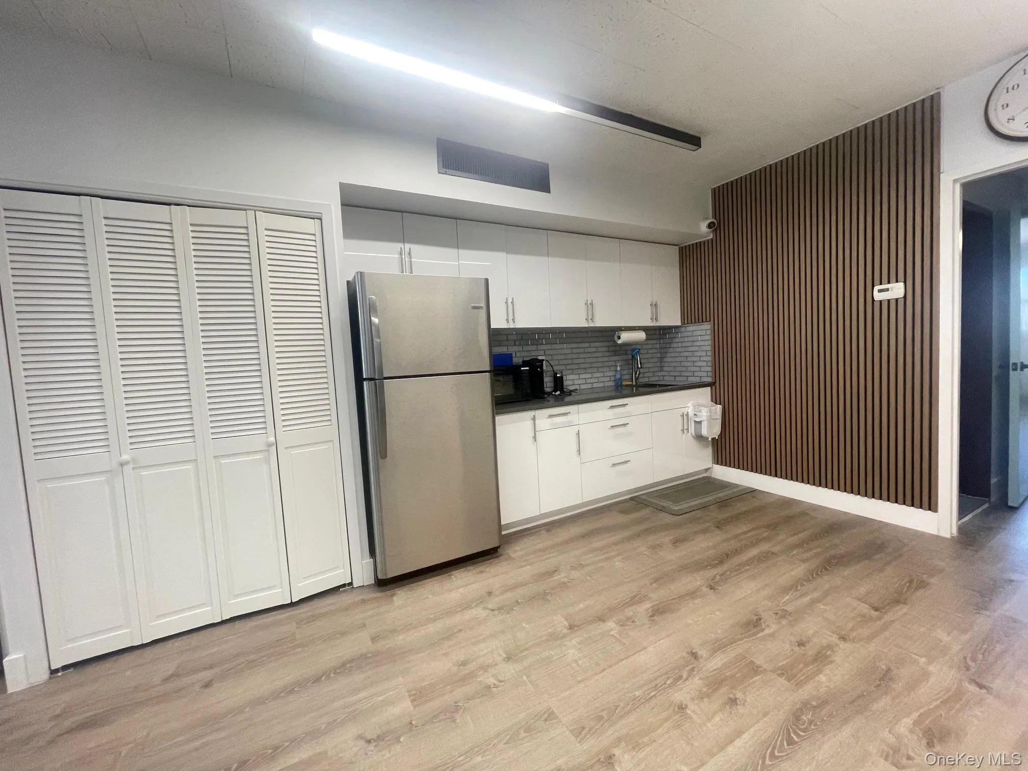 Kitchen featuring white cabinets, freestanding refrigerator, light wood-style floors, dark countertops, and decorative backsplash Kitchen featuring white cabinets, freestanding refrigerator, light wood-style floors, dark countertops, and decorative backsplash