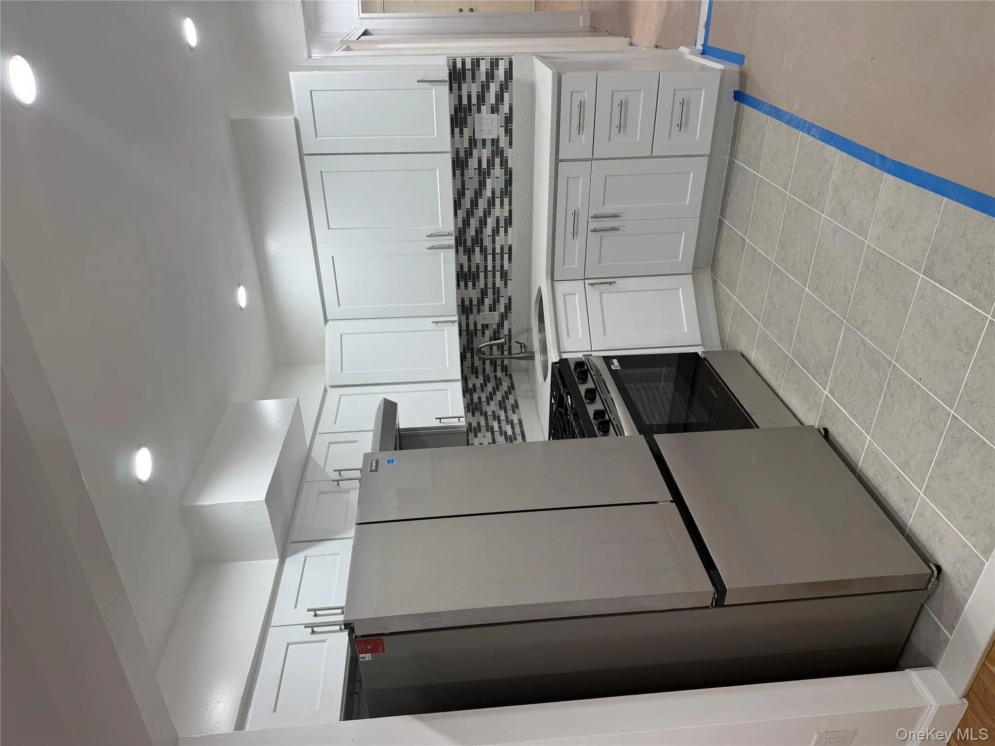 Kitchen featuring stainless steel refrigerator, decorative backsplash, white cabinets, stove, and recessed lighting Kitchen featuring stainless steel refrigerator, decorative backsplash, white cabinets, stove, and recessed lighting