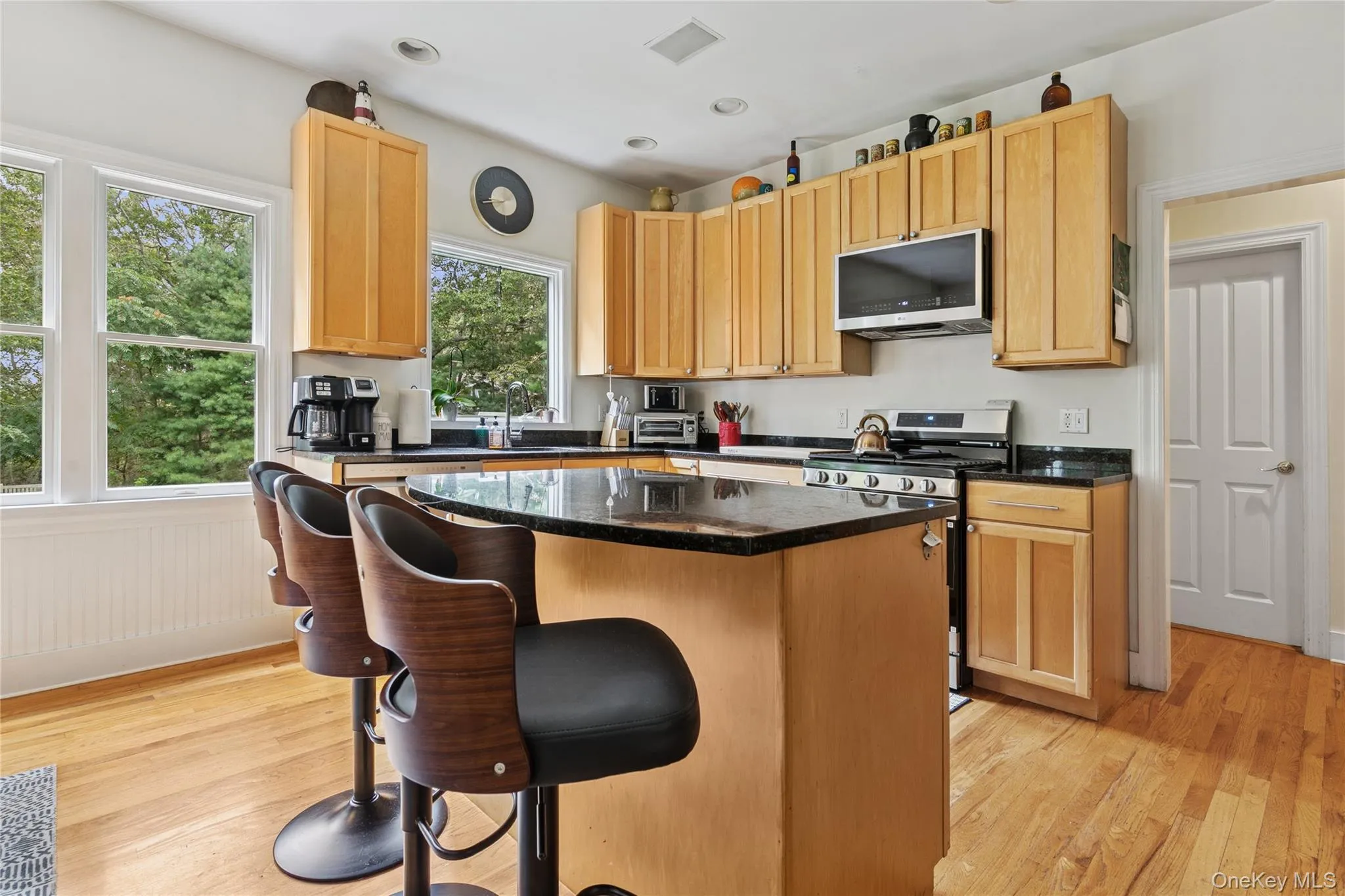 Kitchen featuring a kitchen island, appliances with stainless steel finishes, light wood-type flooring, dark stone counters, and recessed lighting Kitchen featuring a kitchen island, appliances with stainless steel finishes, light wood-type flooring, dark stone counters, and recessed lighting