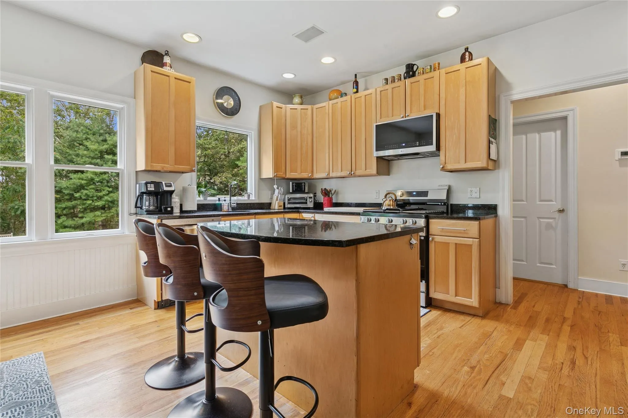 Kitchen with stainless steel appliances, a breakfast bar area, light wood-type flooring, a kitchen island, and dark stone counters Kitchen with stainless steel appliances, a breakfast bar area, light wood-type flooring, a kitchen island, and dark stone counters
