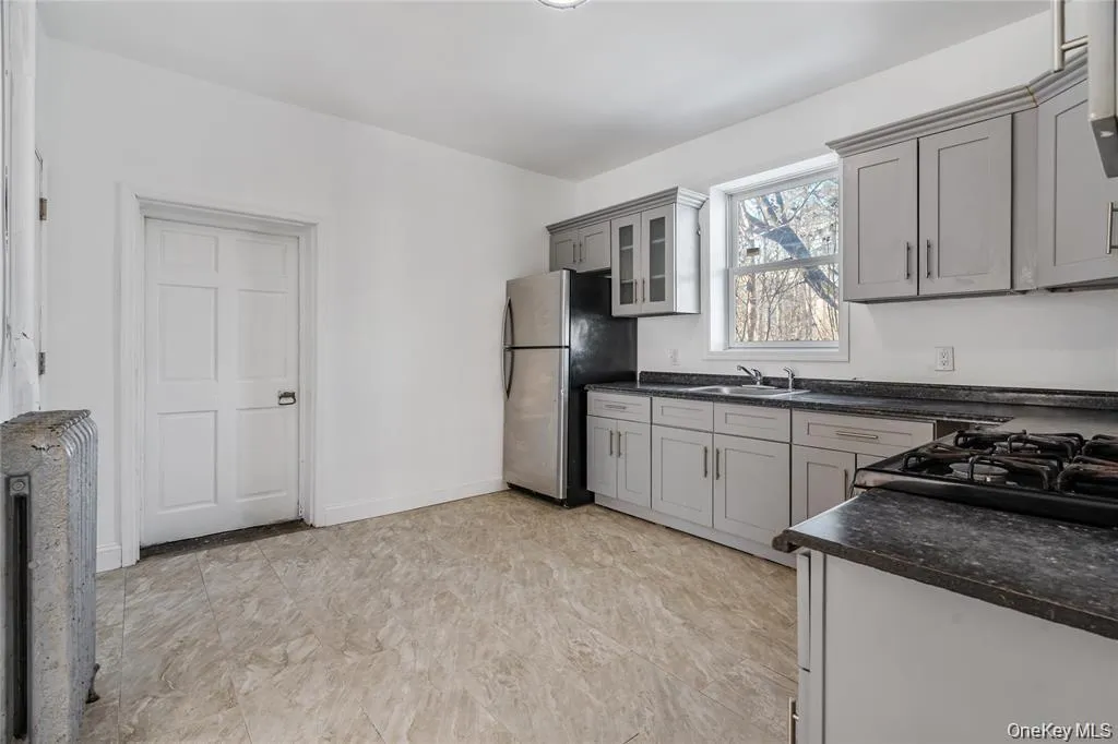 Kitchen featuring dark countertops, gray cabinetry, freestanding refrigerator, and glass insert cabinets Kitchen featuring dark countertops, gray cabinetry, freestanding refrigerator, and glass insert cabinets