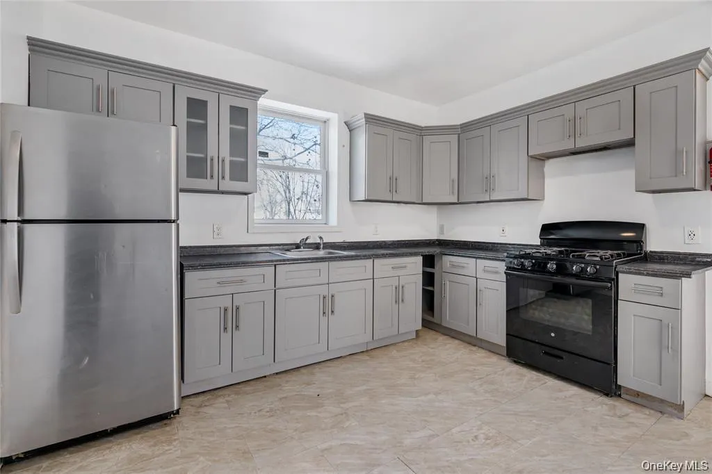 Kitchen featuring freestanding refrigerator, black gas range oven, gray cabinetry, and glass insert cabinets Kitchen featuring freestanding refrigerator, black gas range oven, gray cabinetry, and glass insert cabinets