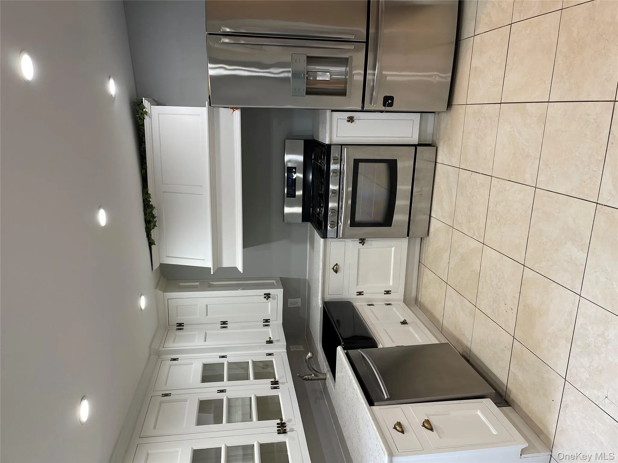 Kitchen with refrigerator, white cabinetry, stainless steel range with gas cooktop, glass insert cabinets, and recessed lighting Kitchen with refrigerator, white cabinetry, stainless steel range with gas cooktop, glass insert cabinets, and recessed lighting