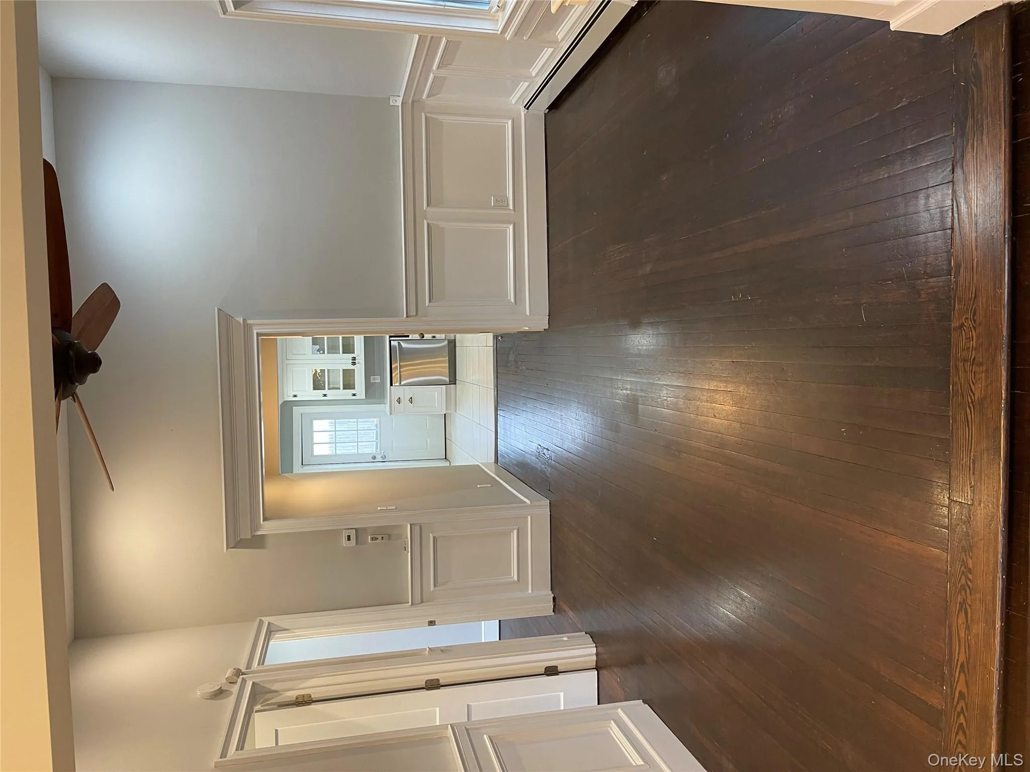 Unfurnished living room featuring a decorative wall, dark wood finished floors, a wainscoted wall, a baseboard heating unit, and a ceiling fan Unfurnished living room featuring a decorative wall, dark wood finished floors, a wainscoted wall, a baseboard heating unit, and a ceiling fan