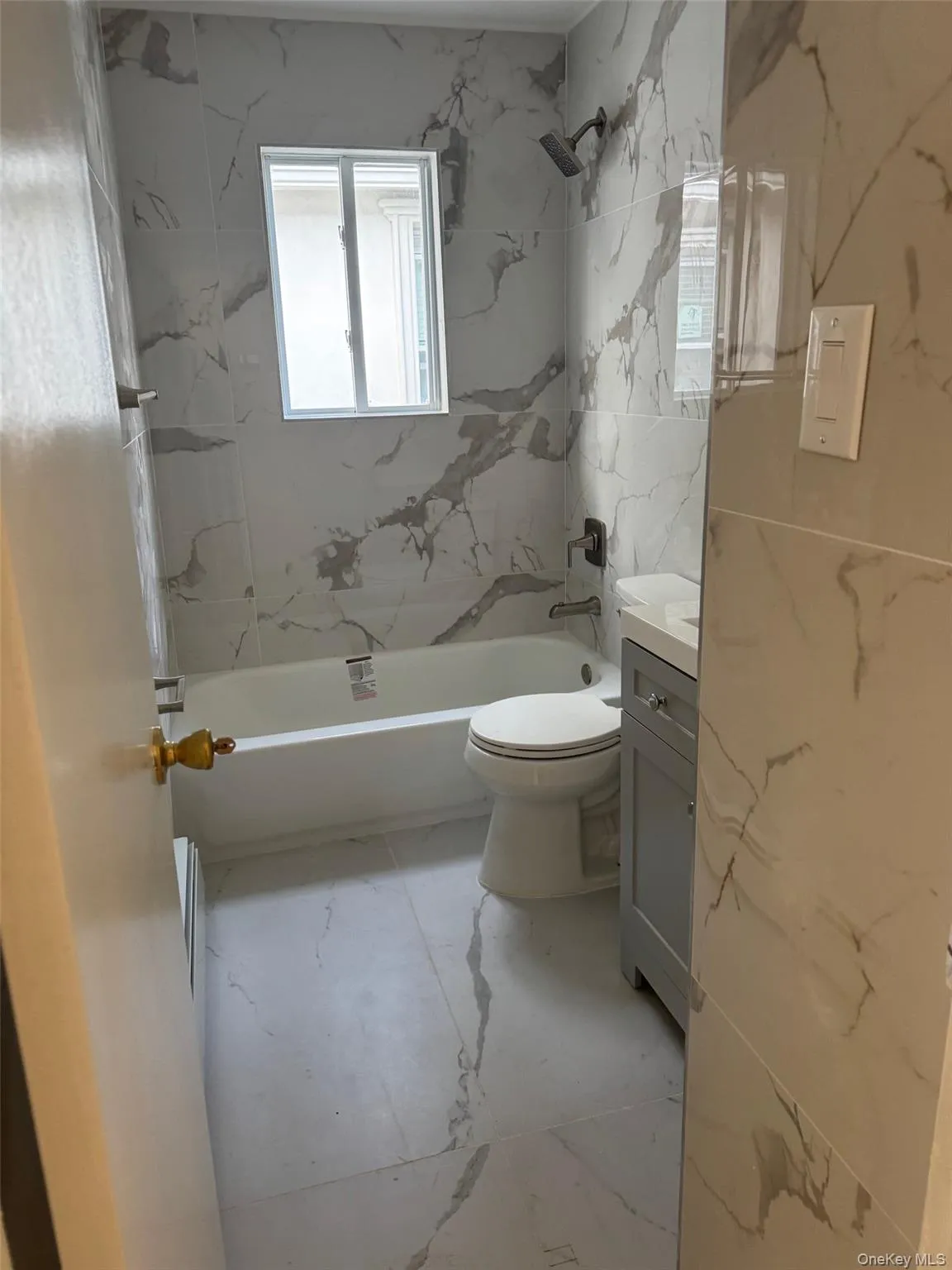Full bath featuring light marble finish floors,  shower combination, vanity, and tile walls Full bath featuring light marble finish floors,  shower combination, vanity, and tile walls