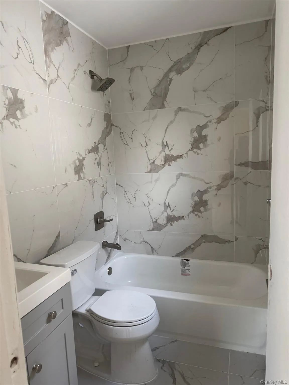 Bathroom featuring vanity, tile walls, shower / tub combination, and marble look tiles Bathroom featuring vanity, tile walls, shower / tub combination, and marble look tiles