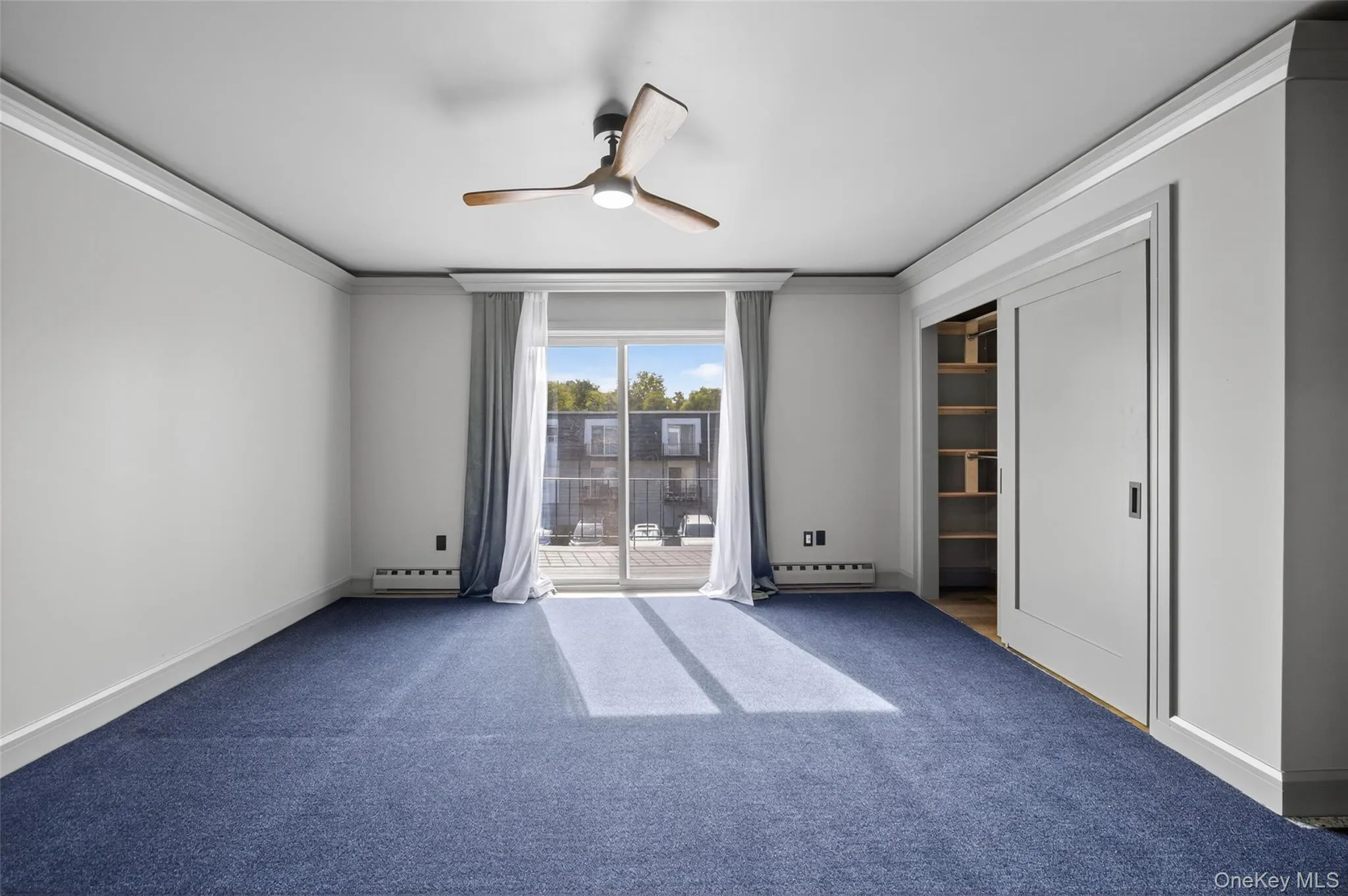 Carpeted empty room featuring ornamental molding, ceiling fan, and a baseboard radiator Carpeted empty room featuring ornamental molding, ceiling fan, and a baseboard radiator