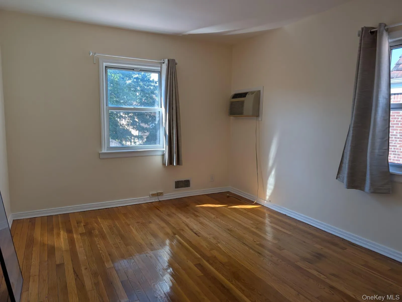 Unfurnished room featuring wood-type flooring, plenty of natural light, and an AC wall unit Unfurnished room featuring wood-type flooring, plenty of natural light, and an AC wall unit