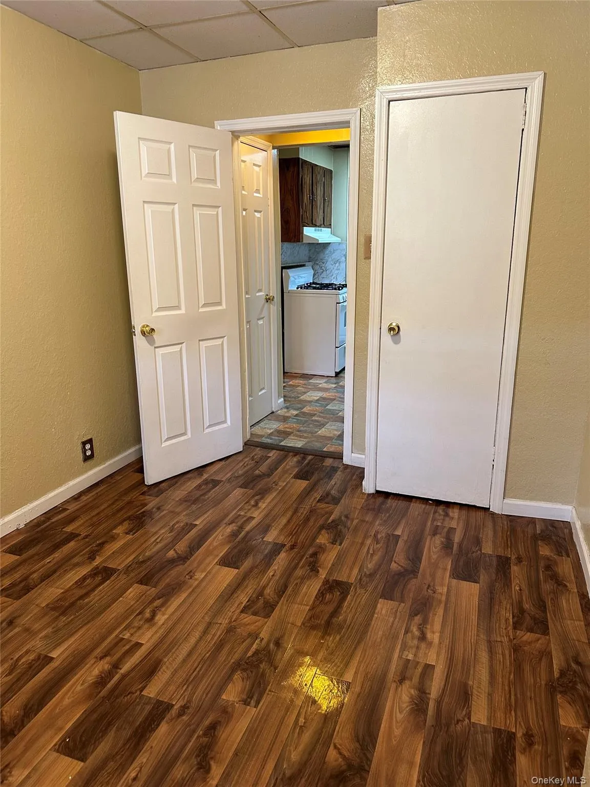 Smaller bedroom with a single closet, dark wood-type flooring, and a drop ceiling Smaller bedroom with a single closet, dark wood-type flooring, and a drop ceiling