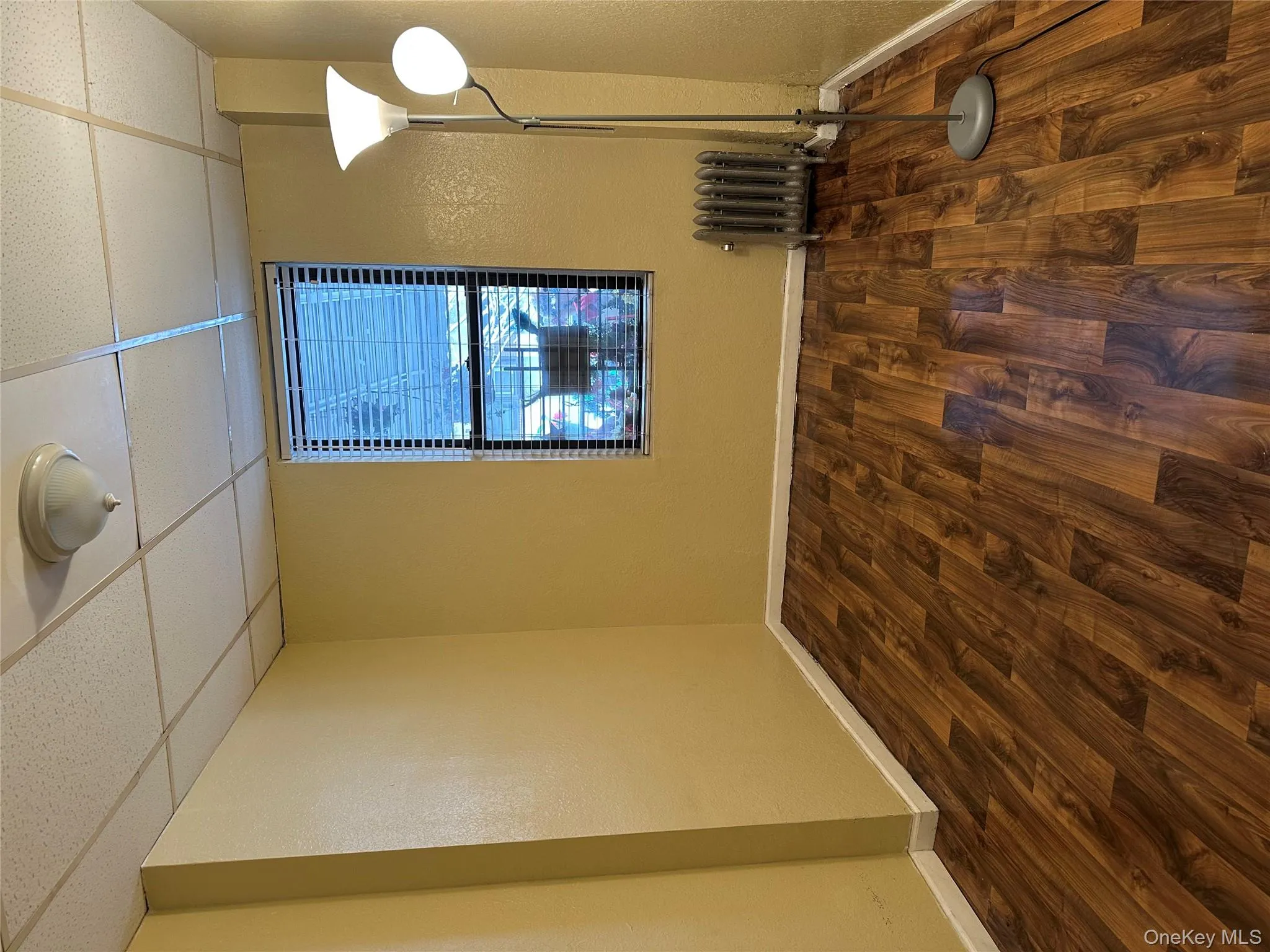 Empty room with dark wood-style flooring, a textured wall, a drop ceiling, and radiator Empty room with dark wood-style flooring, a textured wall, a drop ceiling, and radiator