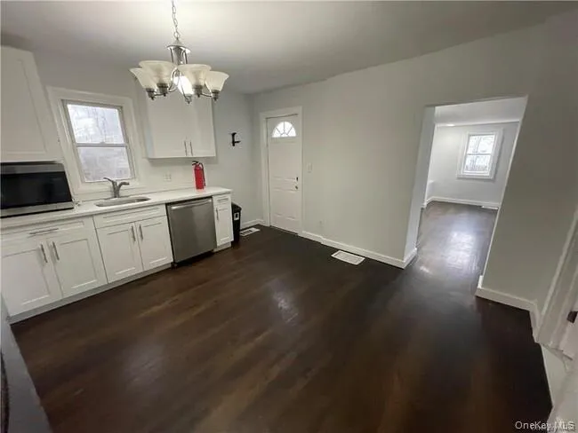 Kitchen with white cabinets, stainless steel appliances, a chandelier, dark wood-type flooring, and pendant lighting Kitchen with white cabinets, stainless steel appliances, a chandelier, dark wood-type flooring, and pendant lighting