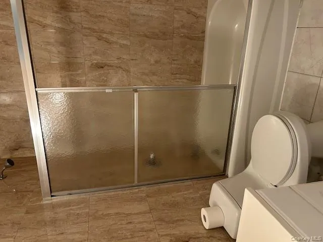 Full bath featuring tile walls, shower / bath combination with glass door, vanity, and tile patterned flooring Full bath featuring tile walls, shower / bath combination with glass door, vanity, and tile patterned flooring