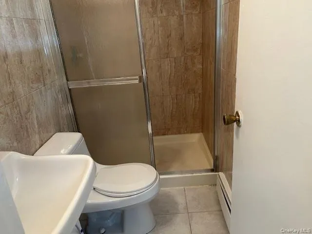 Bathroom with light tile patterned flooring, a stall shower, a baseboard radiator, and tile walls Bathroom with light tile patterned flooring, a stall shower, a baseboard radiator, and tile walls