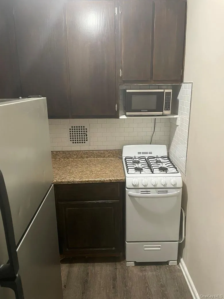 Kitchen featuring dark brown cabinets, white appliances, tasteful backsplash, and dark wood-type flooring Kitchen featuring dark brown cabinets, white appliances, tasteful backsplash, and dark wood-type flooring