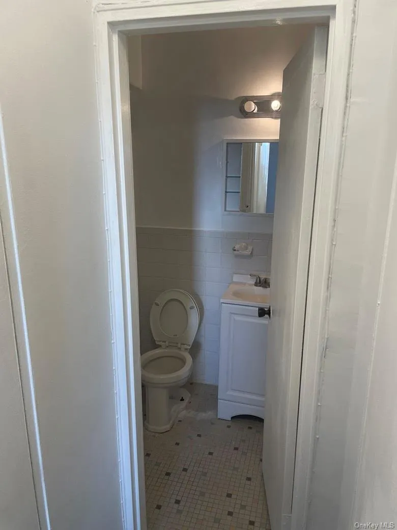 Half bath featuring tile walls, vanity, light tile patterned floors, and wainscoting Half bath featuring tile walls, vanity, light tile patterned floors, and wainscoting