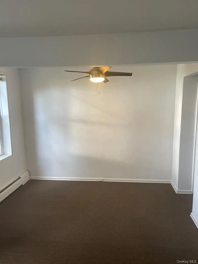 Spare room featuring baseboard heating, a ceiling fan, and dark colored carpet Spare room featuring baseboard heating, a ceiling fan, and dark colored carpet