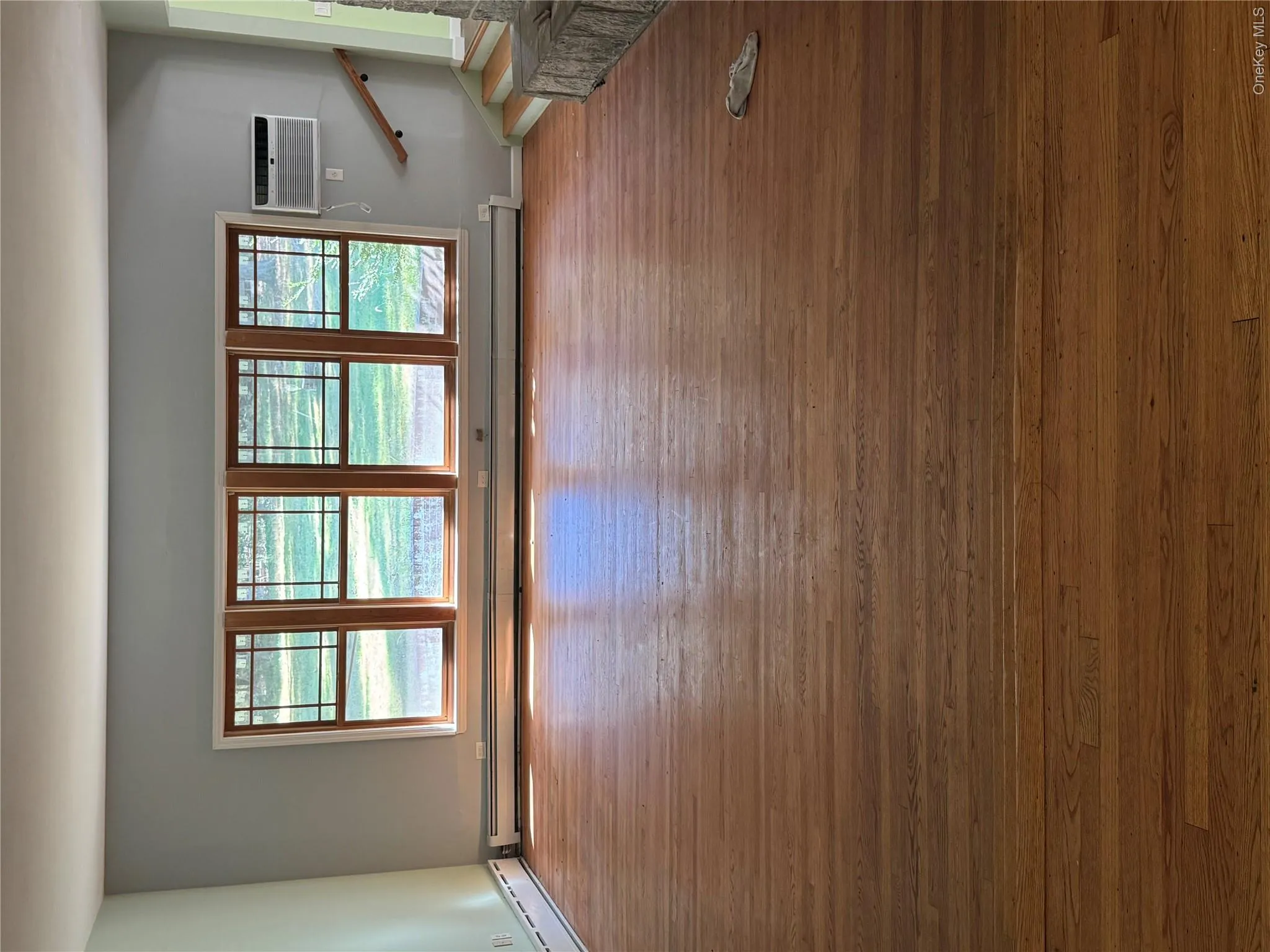 Unfurnished room featuring hardwood / wood-style flooring, baseboard heating, and stairway Unfurnished room featuring hardwood / wood-style flooring, baseboard heating, and stairway