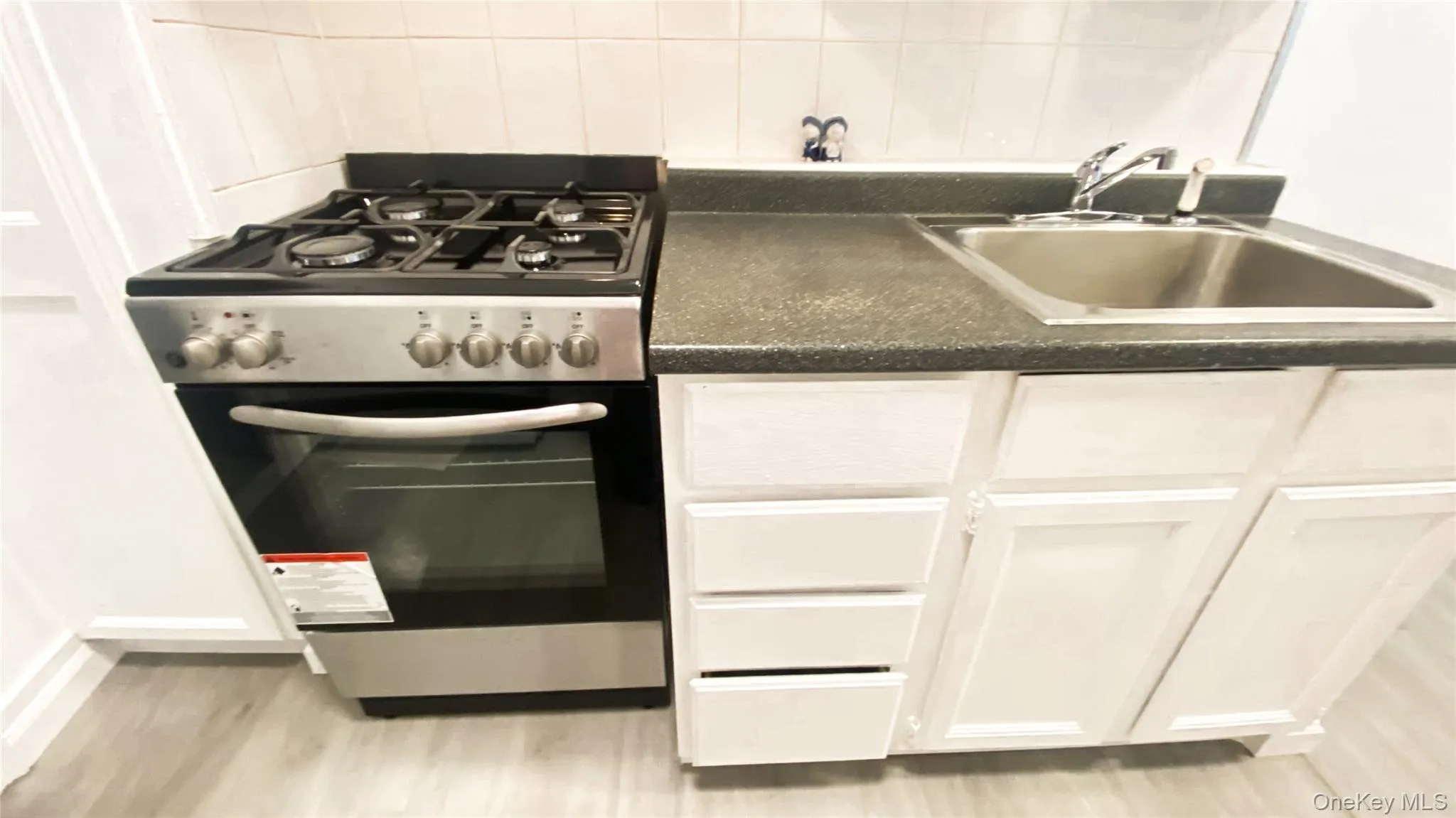 Kitchen with stainless steel gas range oven, white cabinetry, dark countertops, light wood-style flooring, and tasteful backsplash Kitchen with stainless steel gas range oven, white cabinetry, dark countertops, light wood-style flooring, and tasteful backsplash