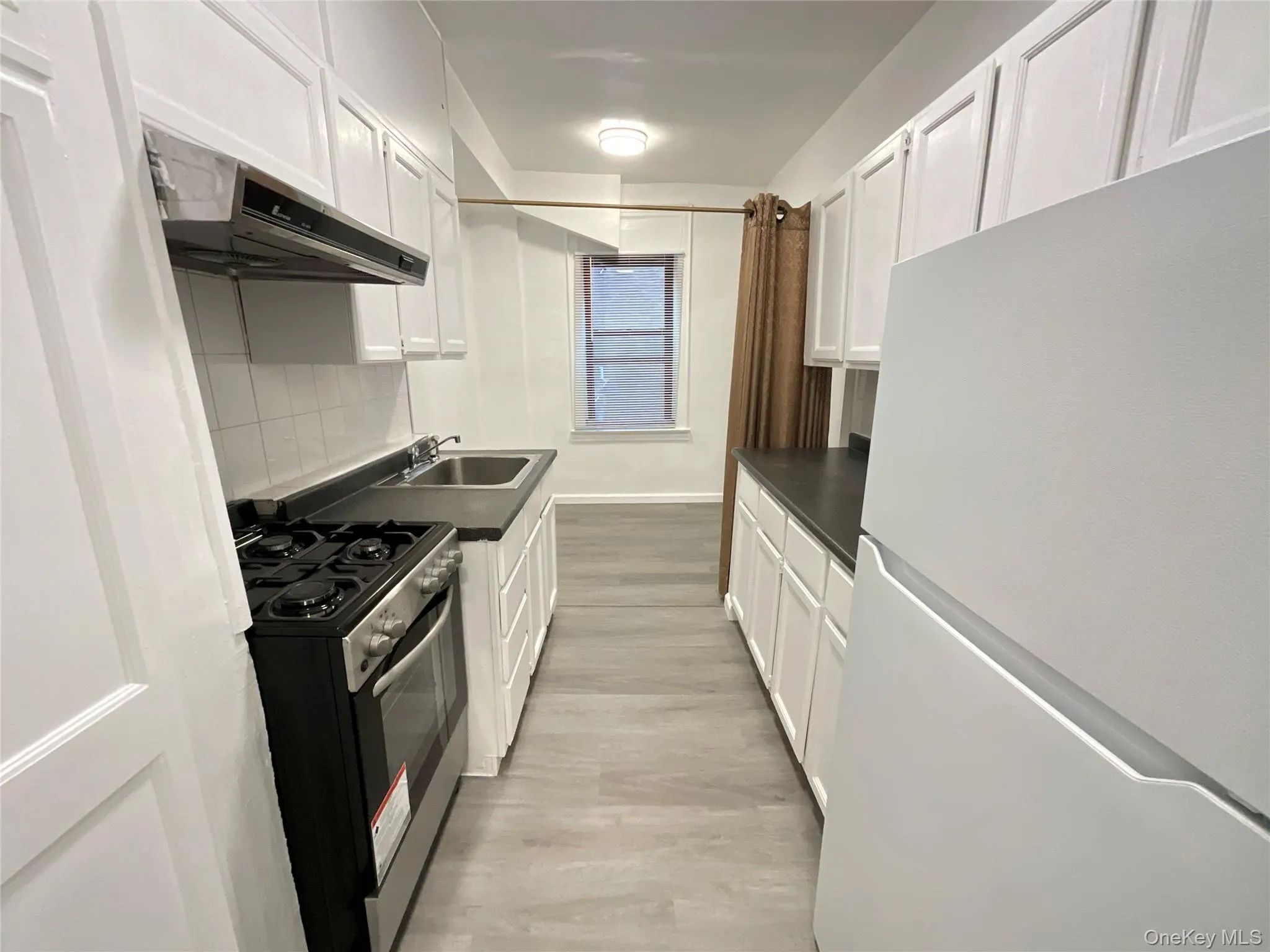 Kitchen with freestanding refrigerator, dark countertops, stainless steel range oven, and white cabinetry Kitchen with freestanding refrigerator, dark countertops, stainless steel range oven, and white cabinetry