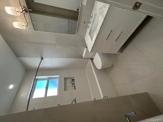 Bathroom featuring tile walls, washtub / shower combination, vanity, and light tile patterned flooring Bathroom featuring tile walls, washtub / shower combination, vanity, and light tile patterned flooring