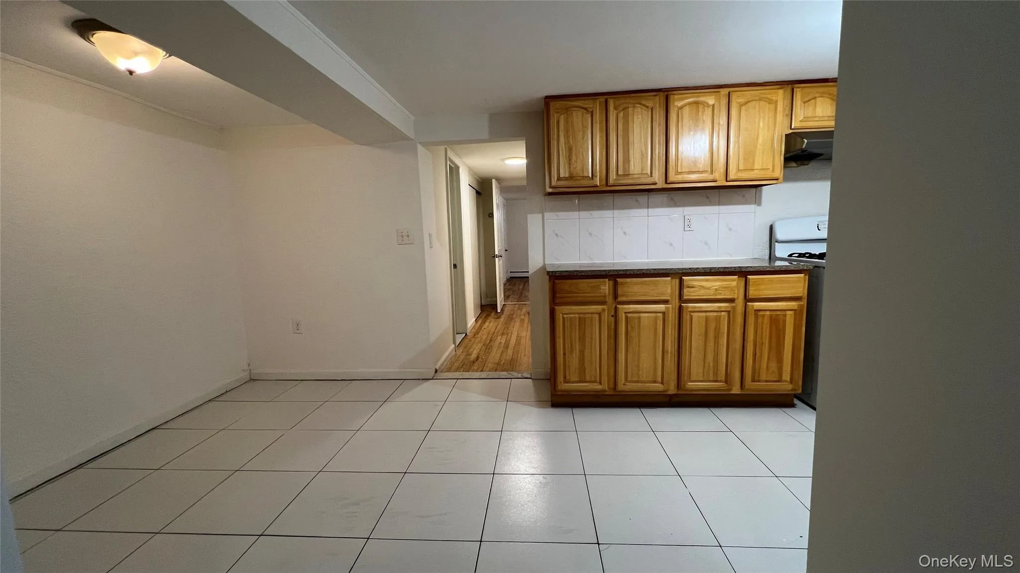 Kitchen featuring brown cabinets, white gas range, light tile patterned flooring, under cabinet range hood, and decorative backsplash Kitchen featuring brown cabinets, white gas range, light tile patterned flooring, under cabinet range hood, and decorative backsplash