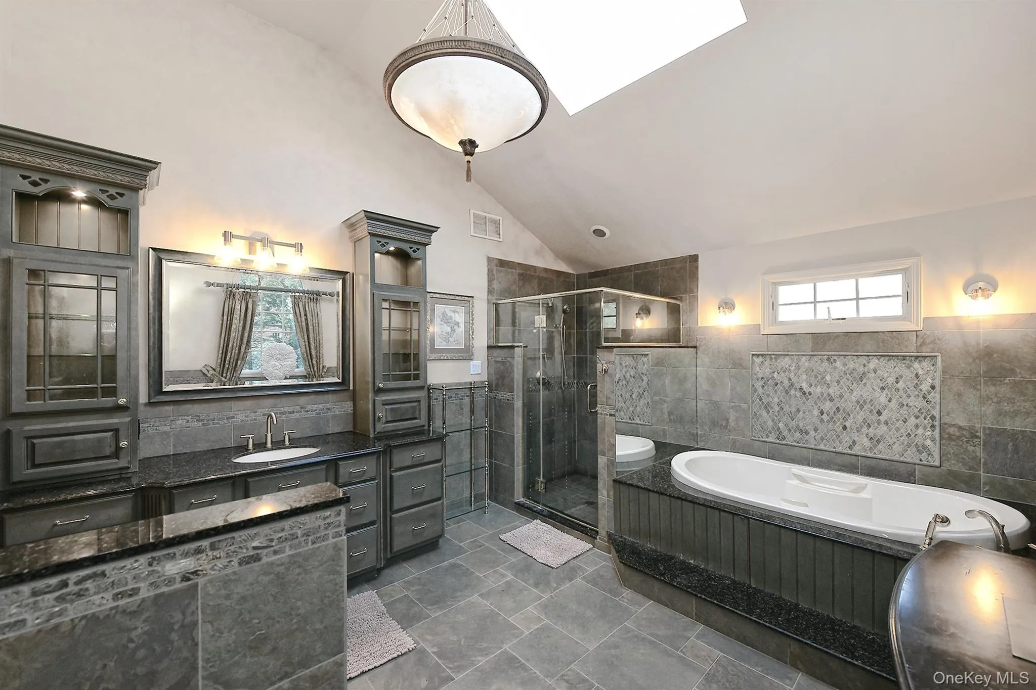 Bathroom with tile walls, vaulted ceiling, vanity, a garden tub, and a shower stall Bathroom with tile walls, vaulted ceiling, vanity, a garden tub, and a shower stall