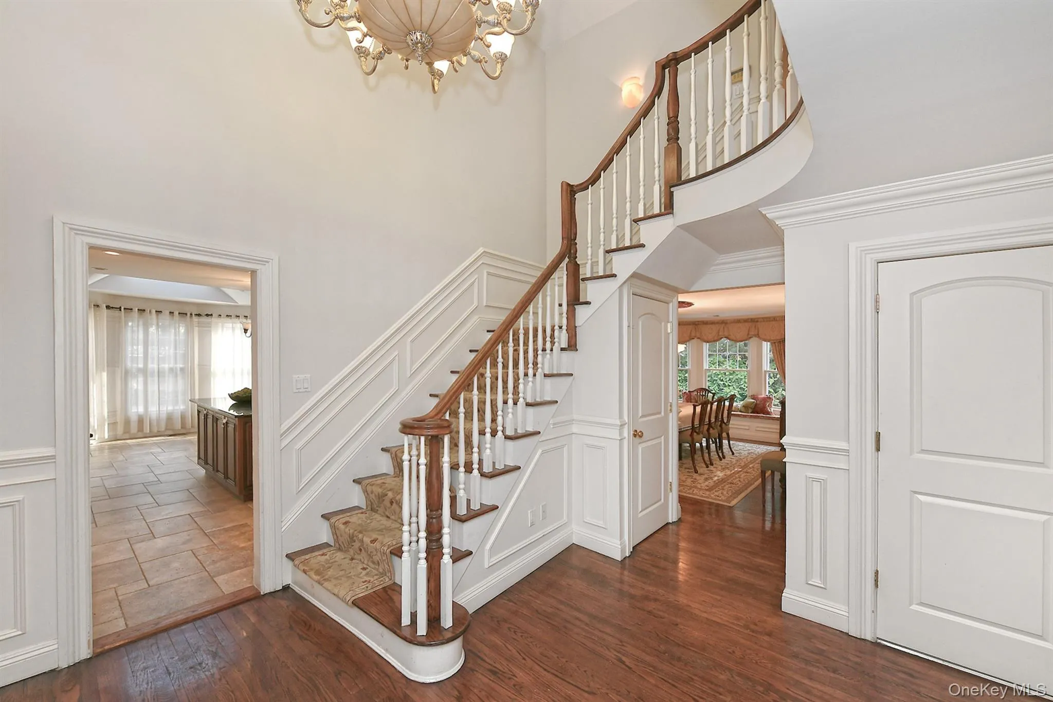 Staircase featuring a decorative wall, wood finished floors, a wainscoted wall, a chandelier, and a towering ceiling Staircase featuring a decorative wall, wood finished floors, a wainscoted wall, a chandelier, and a towering ceiling