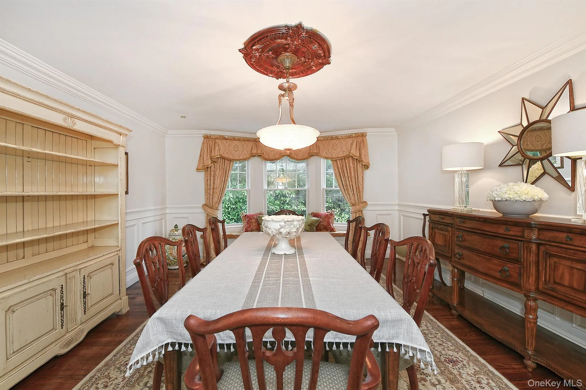 Dining area featuring ornamental molding, dark wood-style flooring, a wainscoted wall, and a decorative wall Dining area featuring ornamental molding, dark wood-style flooring, a wainscoted wall, and a decorative wall