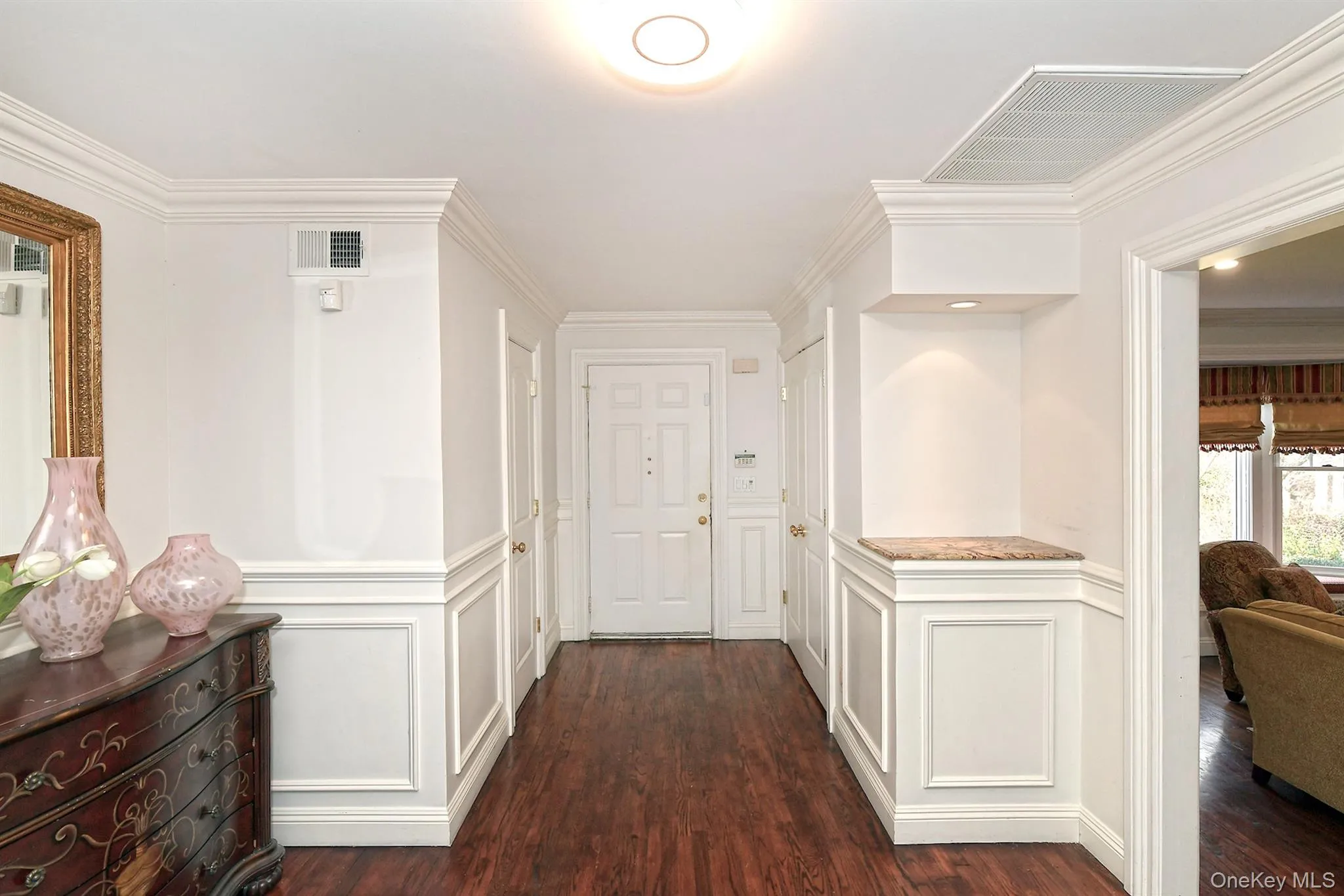 Hall featuring crown molding, dark wood finished floors, a decorative wall, and wainscoting Hall featuring crown molding, dark wood finished floors, a decorative wall, and wainscoting