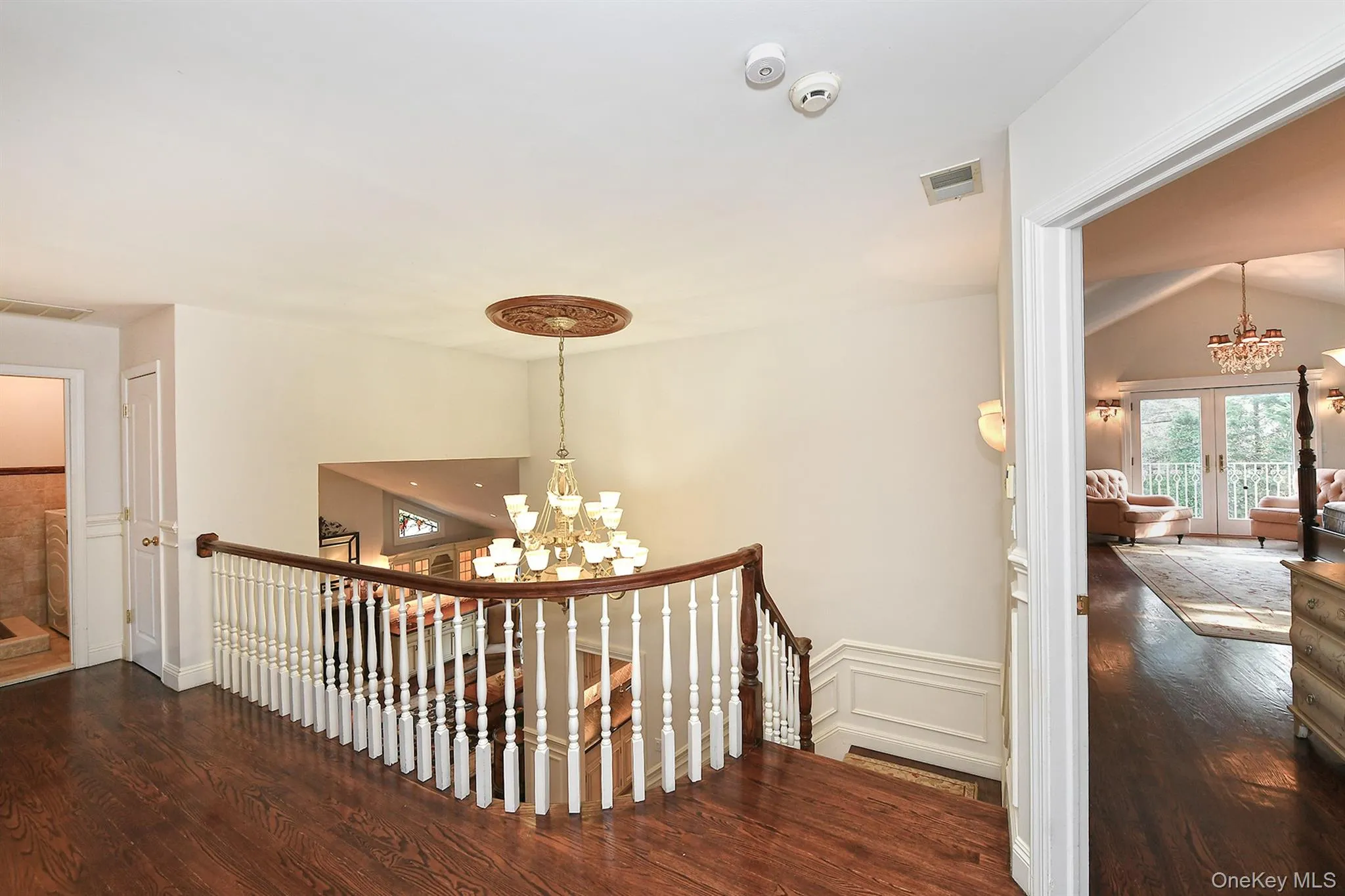 Corridor featuring a chandelier, an upstairs landing, dark wood-style flooring, french doors, and wainscoting Corridor featuring a chandelier, an upstairs landing, dark wood-style flooring, french doors, and wainscoting