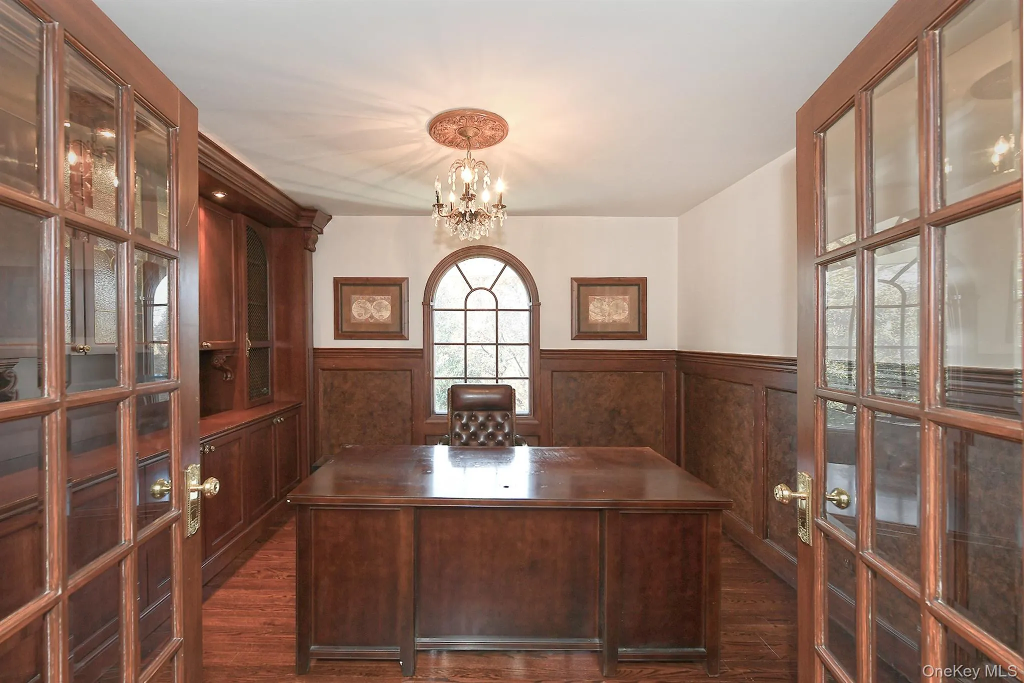 Unfurnished office featuring a wainscoted wall, dark wood-style flooring, a chandelier, a decorative wall, and french doors Unfurnished office featuring a wainscoted wall, dark wood-style flooring, a chandelier, a decorative wall, and french doors