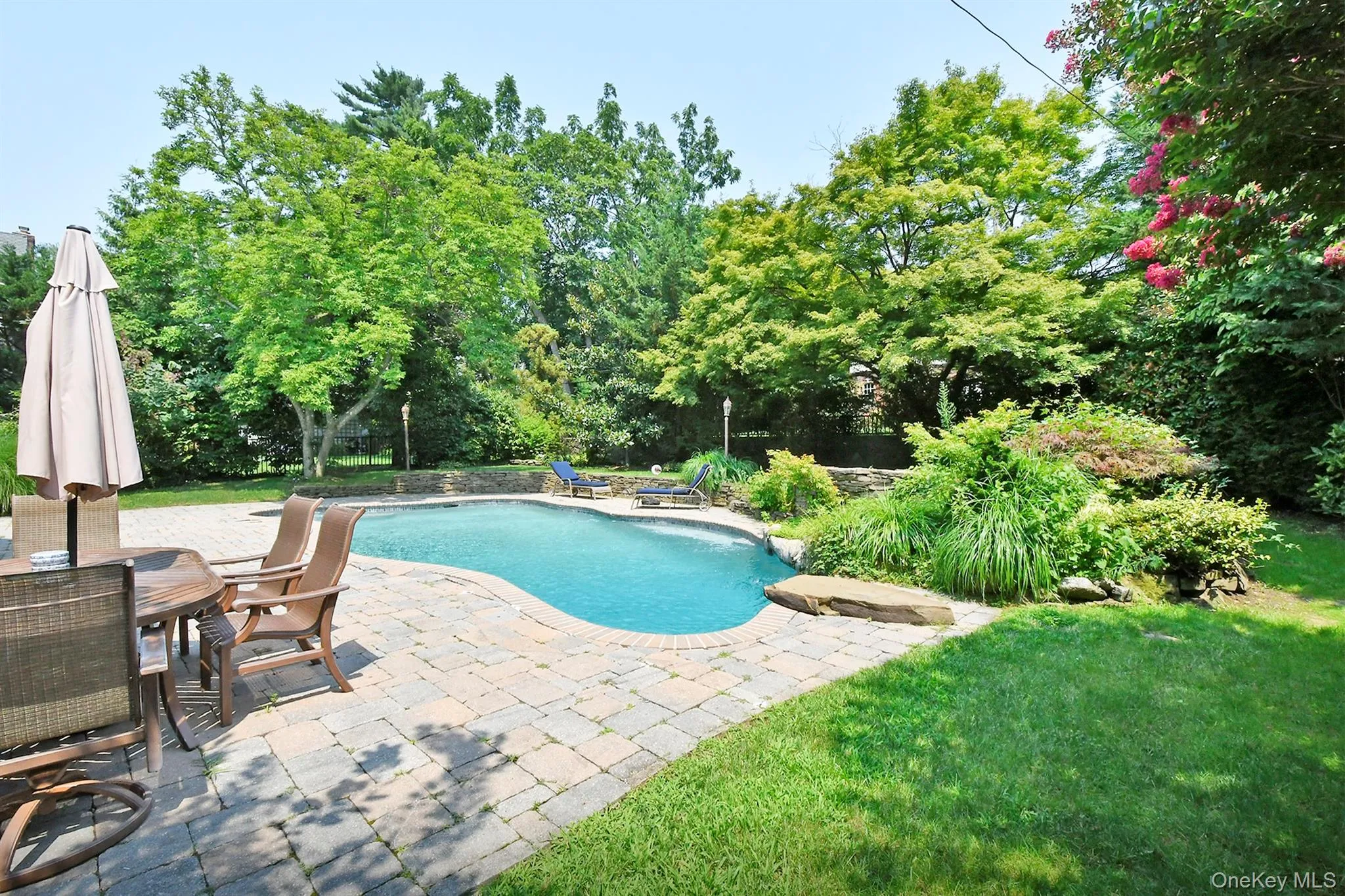 Swimming pool with a patio, a lawn, outdoor dining space, and view of scattered trees Swimming pool with a patio, a lawn, outdoor dining space, and view of scattered trees