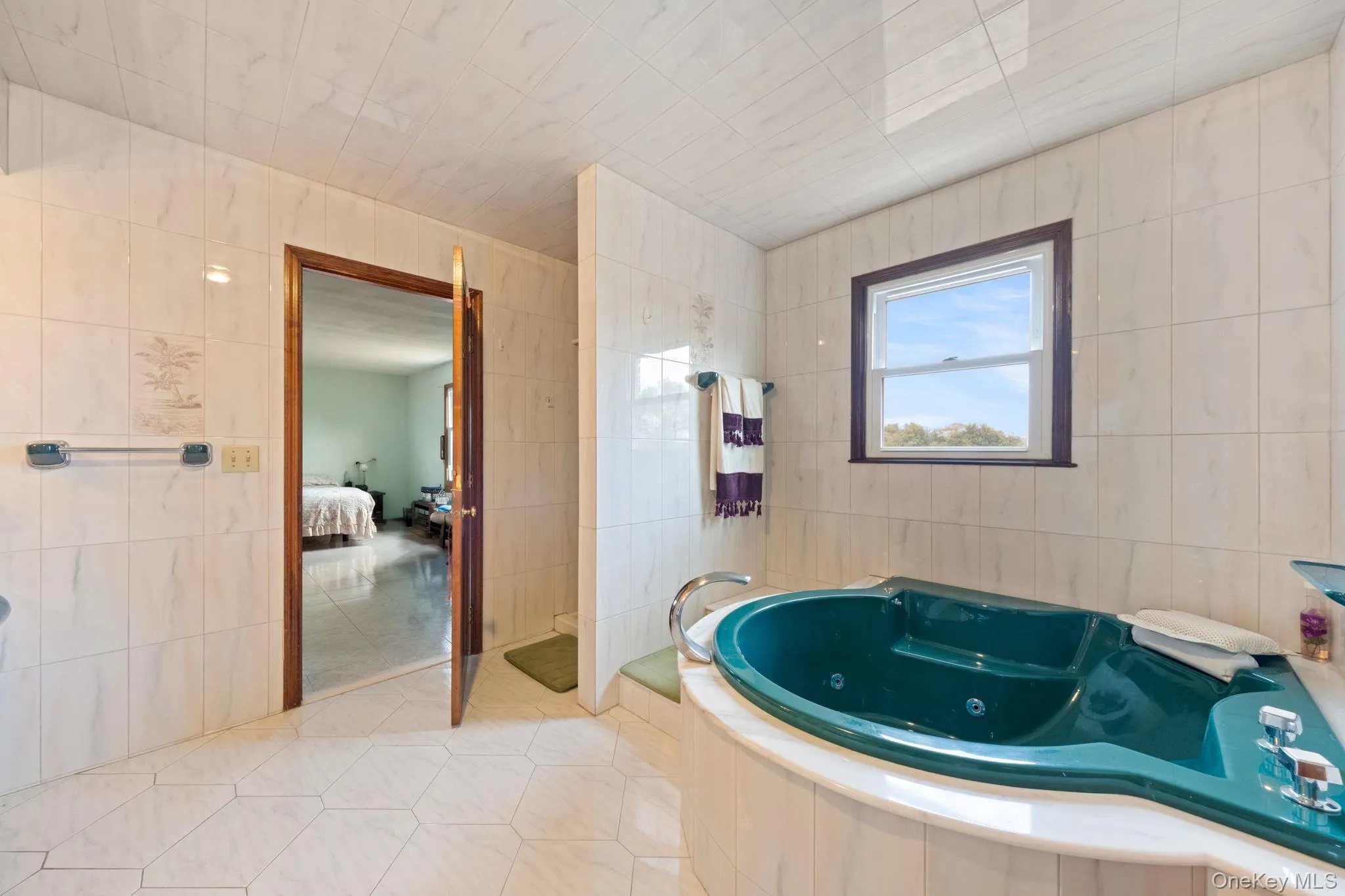 Bathroom featuring tile walls, connected bathroom, a jetted tub, tile patterned flooring, and tiled shower Bathroom featuring tile walls, connected bathroom, a jetted tub, tile patterned flooring, and tiled shower