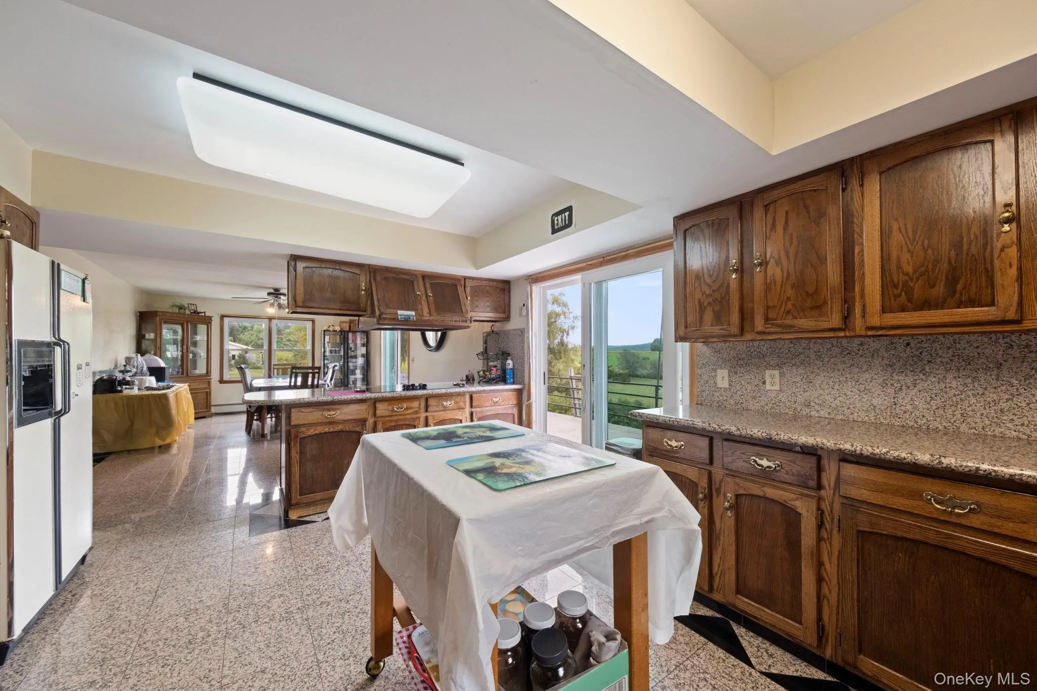 Kitchen featuring a peninsula, granite tiled floors, white fridge with ice dispenser, a ceiling fan, and decorative backsplash Kitchen featuring a peninsula, granite tiled floors, white fridge with ice dispenser, a ceiling fan, and decorative backsplash