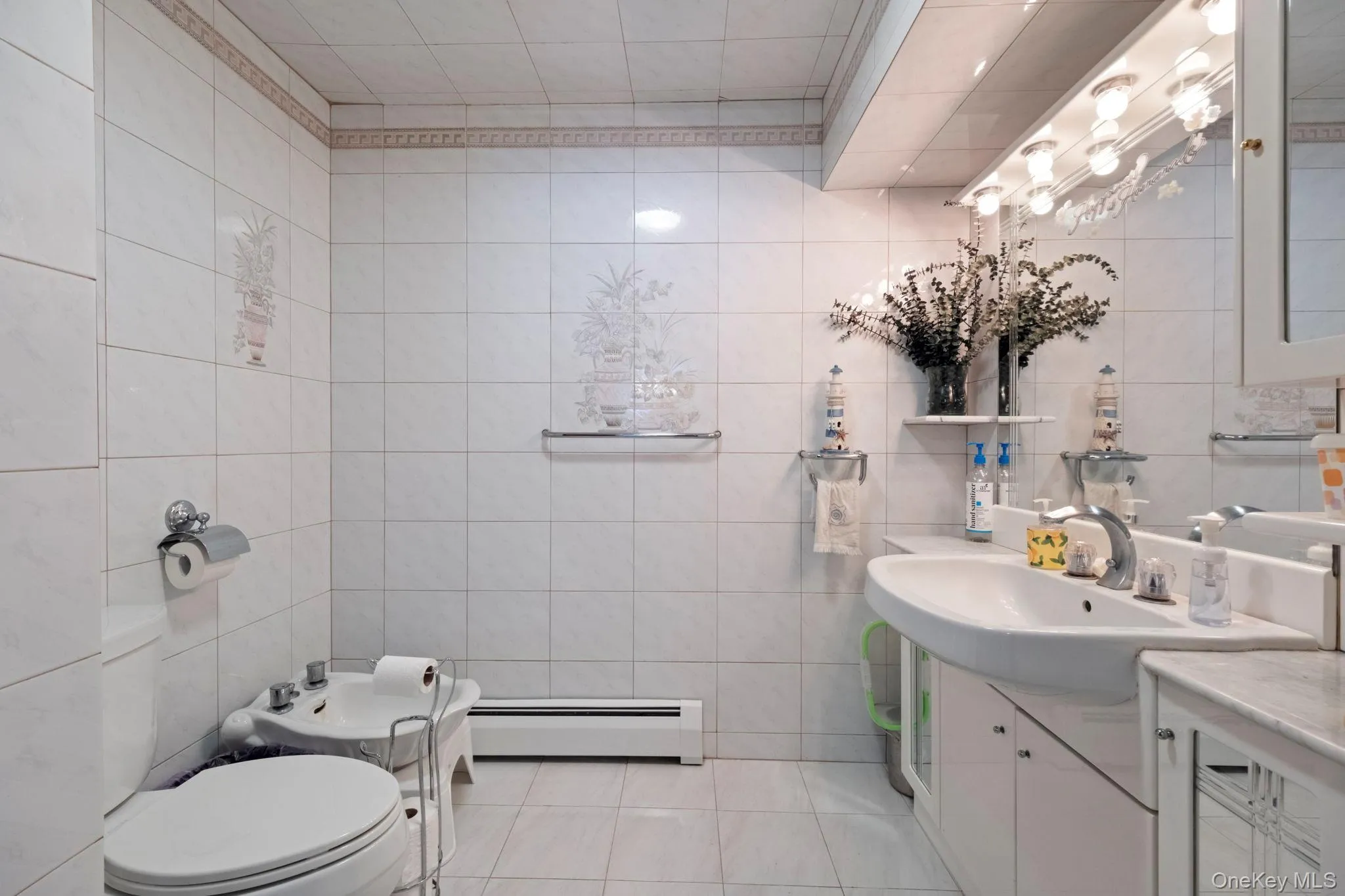 Bathroom featuring tile walls, vanity, light tile patterned floors, a baseboard heating unit, and a bidet Bathroom featuring tile walls, vanity, light tile patterned floors, a baseboard heating unit, and a bidet