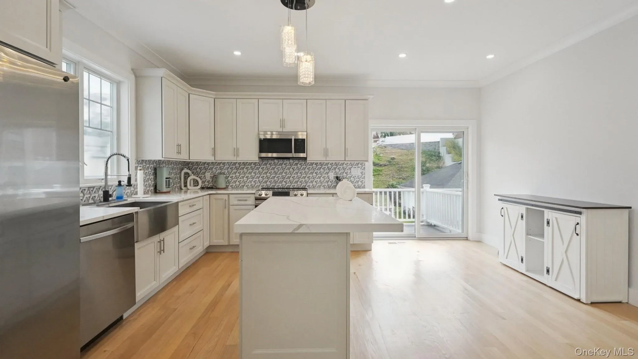 Kitchen with stainless steel appliances, decorative backsplash, a center island, light wood-style flooring, and ornamental molding Kitchen with stainless steel appliances, decorative backsplash, a center island, light wood-style flooring, and ornamental molding