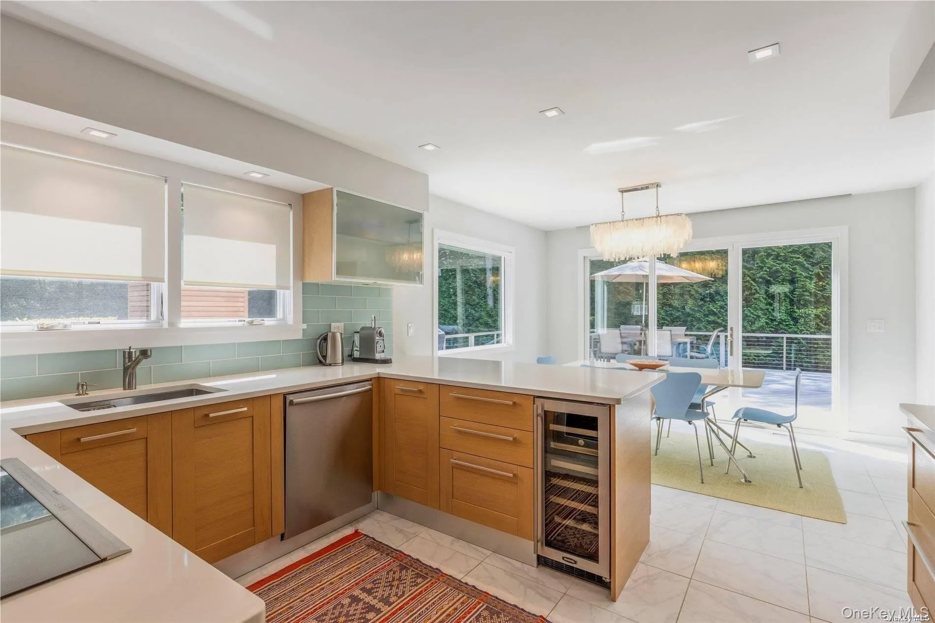 Kitchen with light marble finish floors, hanging light fixtures, backsplash, a peninsula, and black electric stovetop Kitchen with light marble finish floors, hanging light fixtures, backsplash, a peninsula, and black electric stovetop