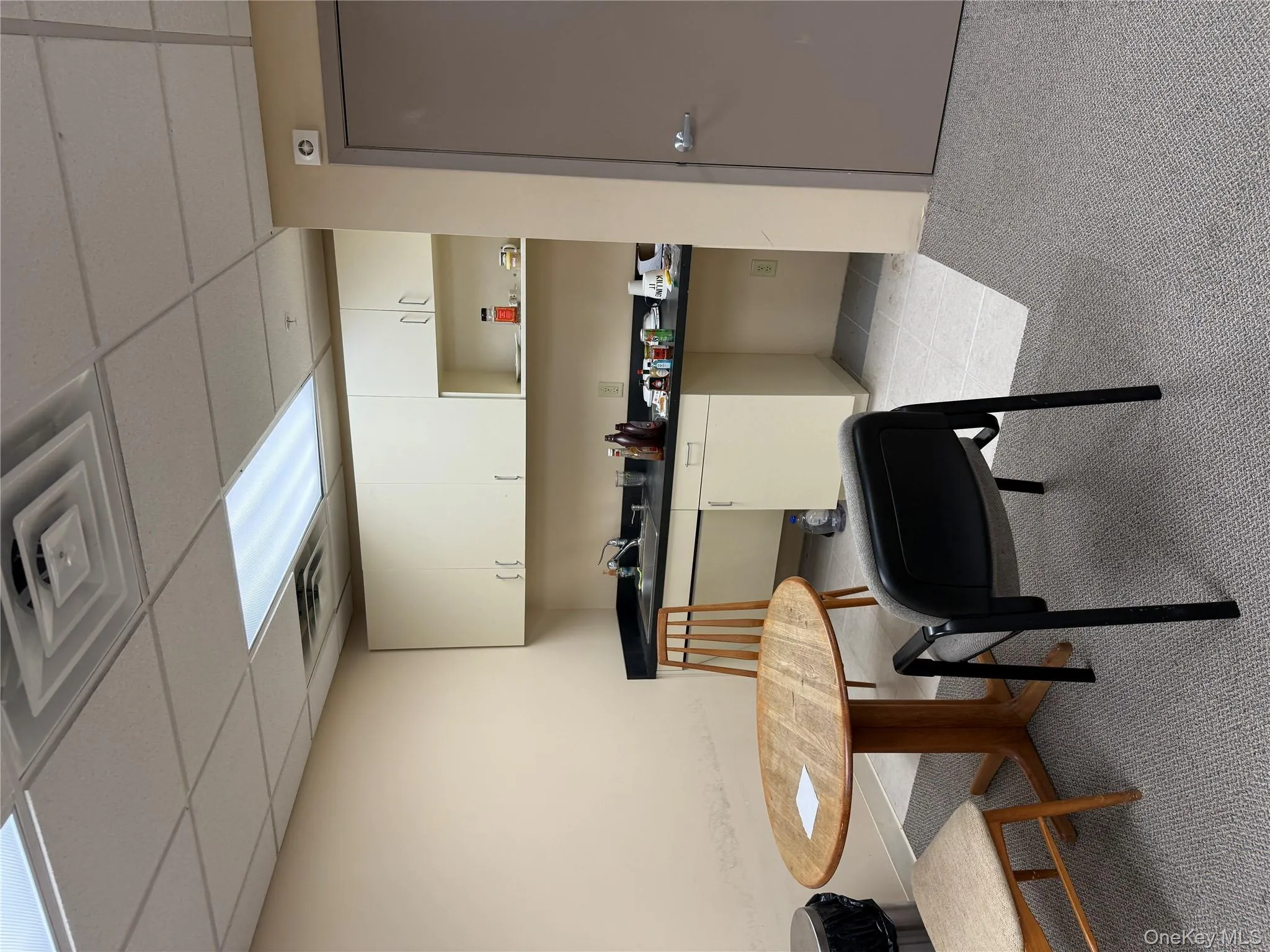 Kitchen with dark countertops, a paneled ceiling, light tile patterned floors, white cabinets, and light carpet Kitchen with dark countertops, a paneled ceiling, light tile patterned floors, white cabinets, and light carpet