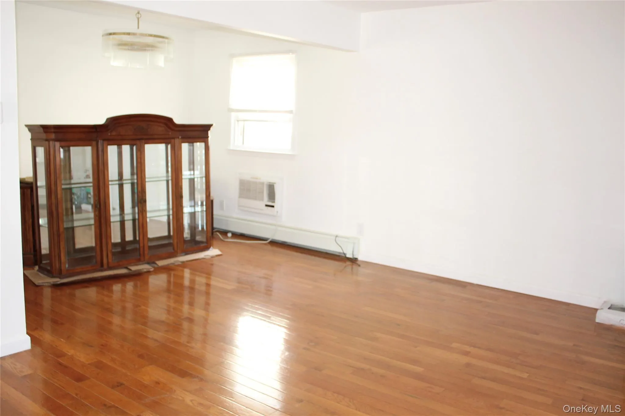 Spare room with wood-type flooring, a baseboard radiator, and a wall mounted air conditioner Spare room with wood-type flooring, a baseboard radiator, and a wall mounted air conditioner