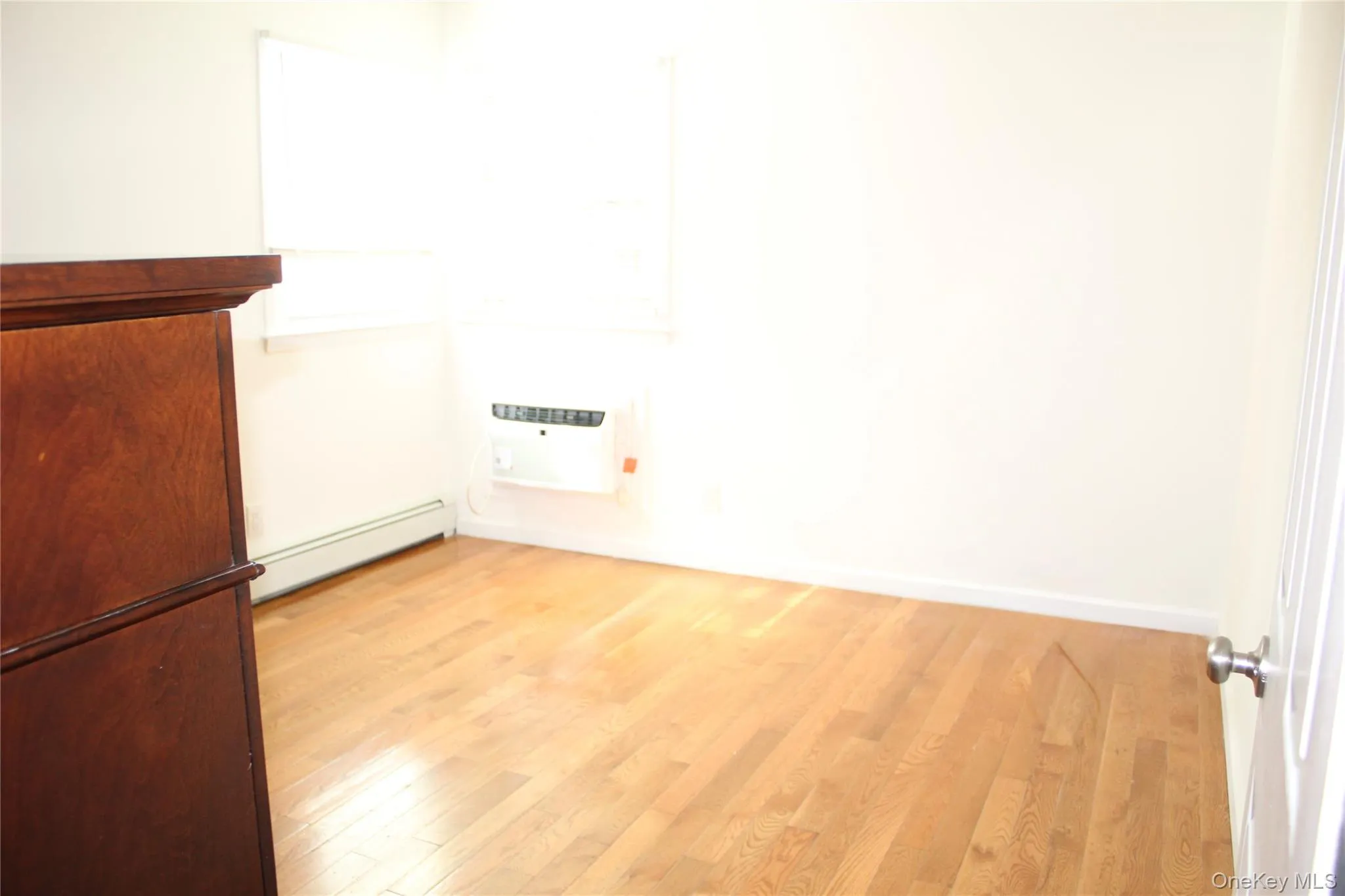 Empty room with light wood-type flooring, a baseboard heating unit, and an AC wall unit Empty room with light wood-type flooring, a baseboard heating unit, and an AC wall unit