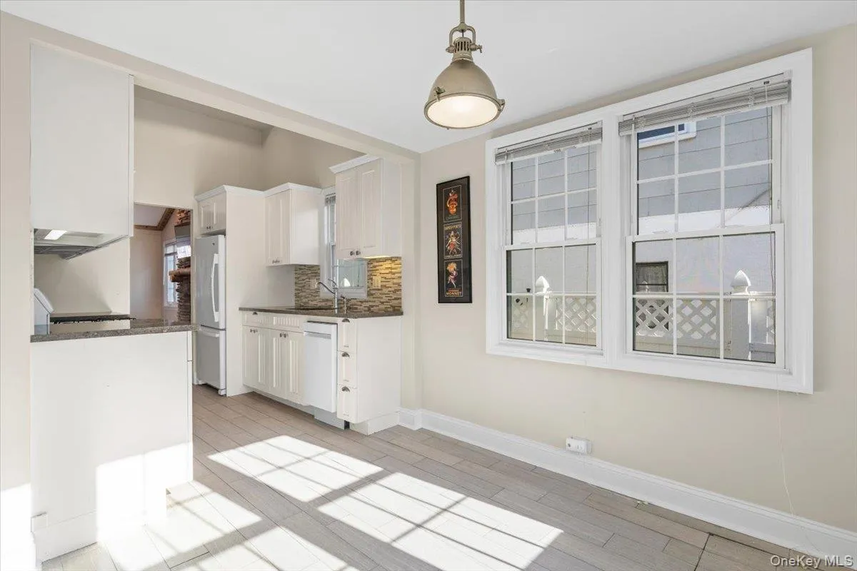 Kitchen with hanging light fixtures, decorative backsplash, white cabinets, white appliances, and light wood-type flooring Kitchen with hanging light fixtures, decorative backsplash, white cabinets, white appliances, and light wood-type flooring