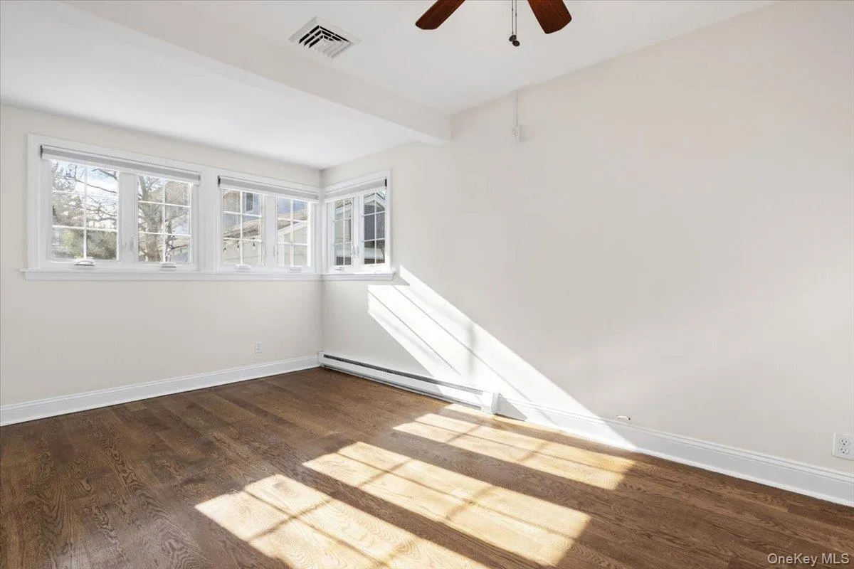 Empty room with dark wood-type flooring, a baseboard heating unit, ceiling fan, and beam ceiling Empty room with dark wood-type flooring, a baseboard heating unit, ceiling fan, and beam ceiling