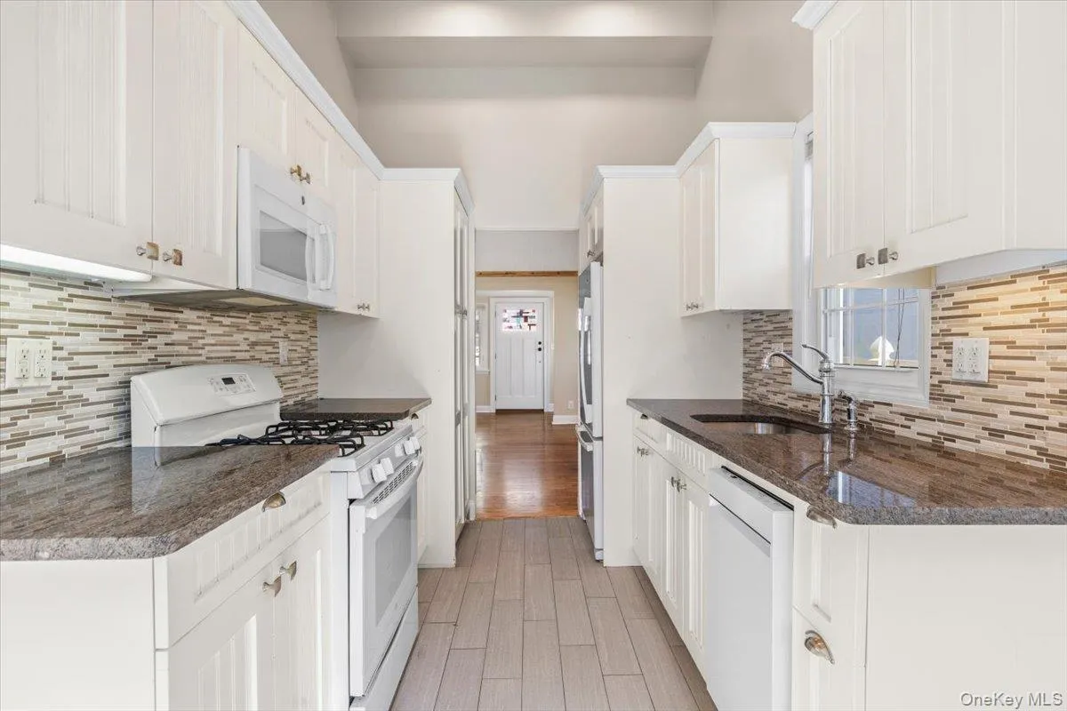 Kitchen with white appliances, tasteful backsplash, light wood-type flooring, and dark stone countertops Kitchen with white appliances, tasteful backsplash, light wood-type flooring, and dark stone countertops